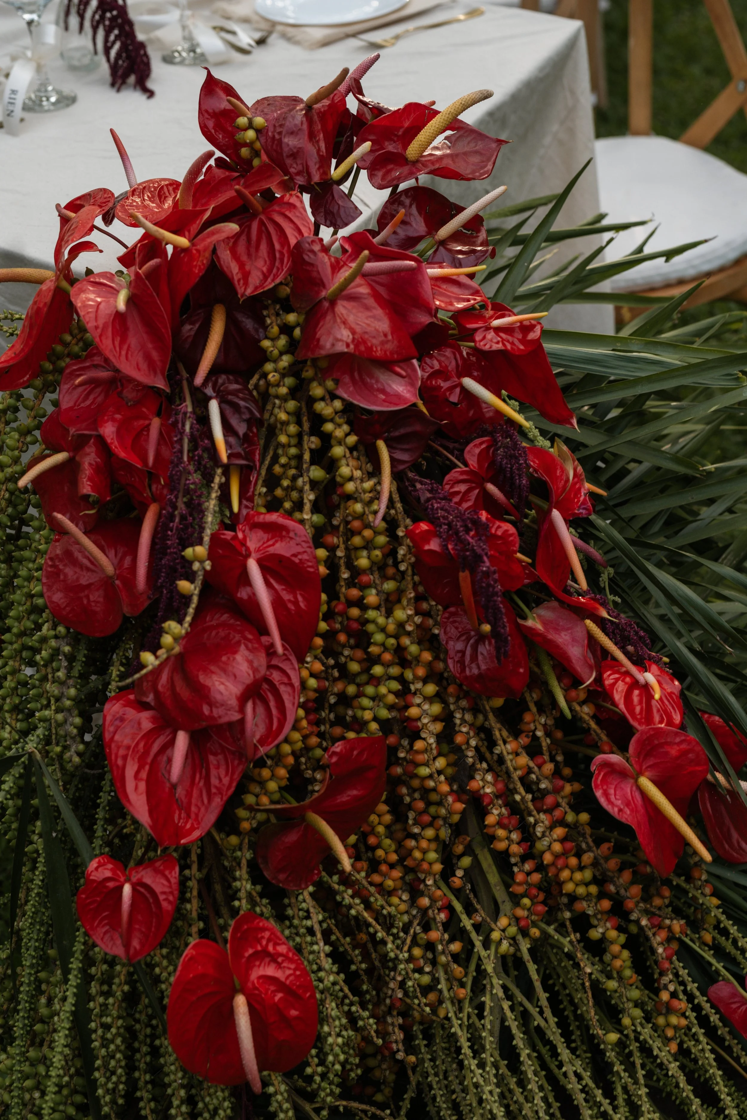 A floral arrangement with red anthuriums, yellow and purple flowers, and green foliage placed on a table covered with a white tablecloth.