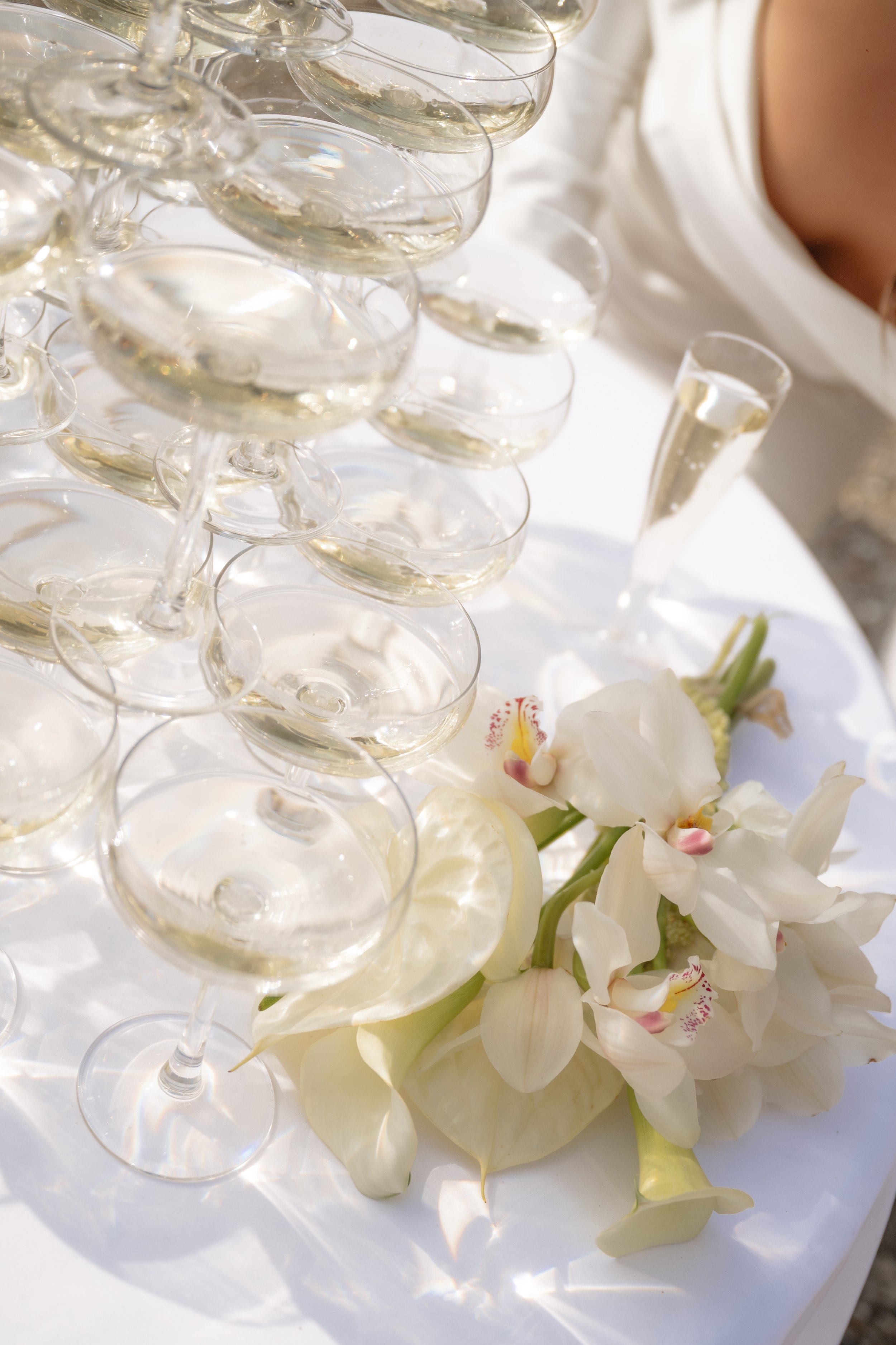 A table with multiple champagne glasses filled with champagne, a bouquet of white flowers, and a champagne flute.