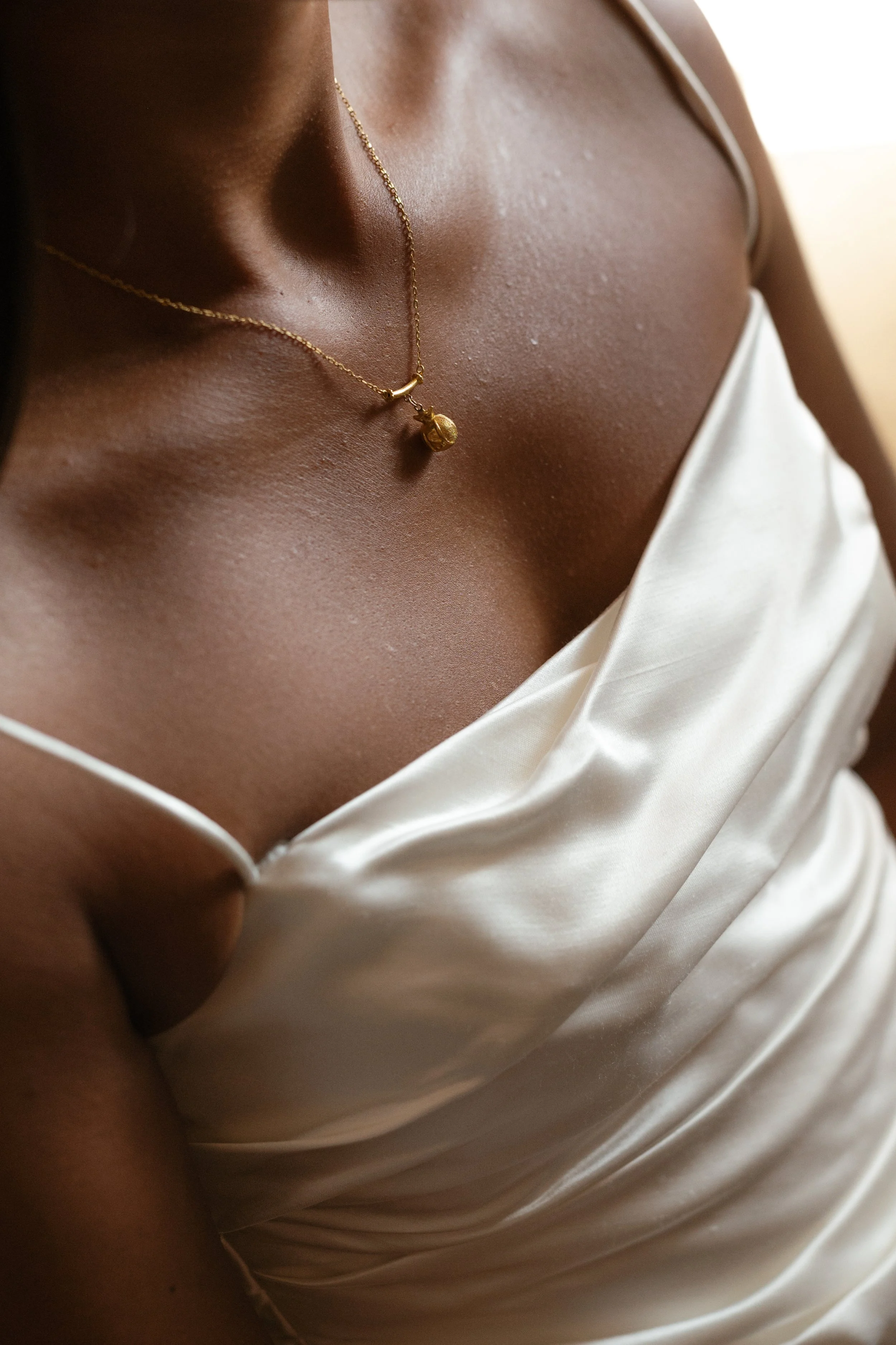 Close-up of a woman's chest wearing a white satin dress and a gold necklace with a pendant.