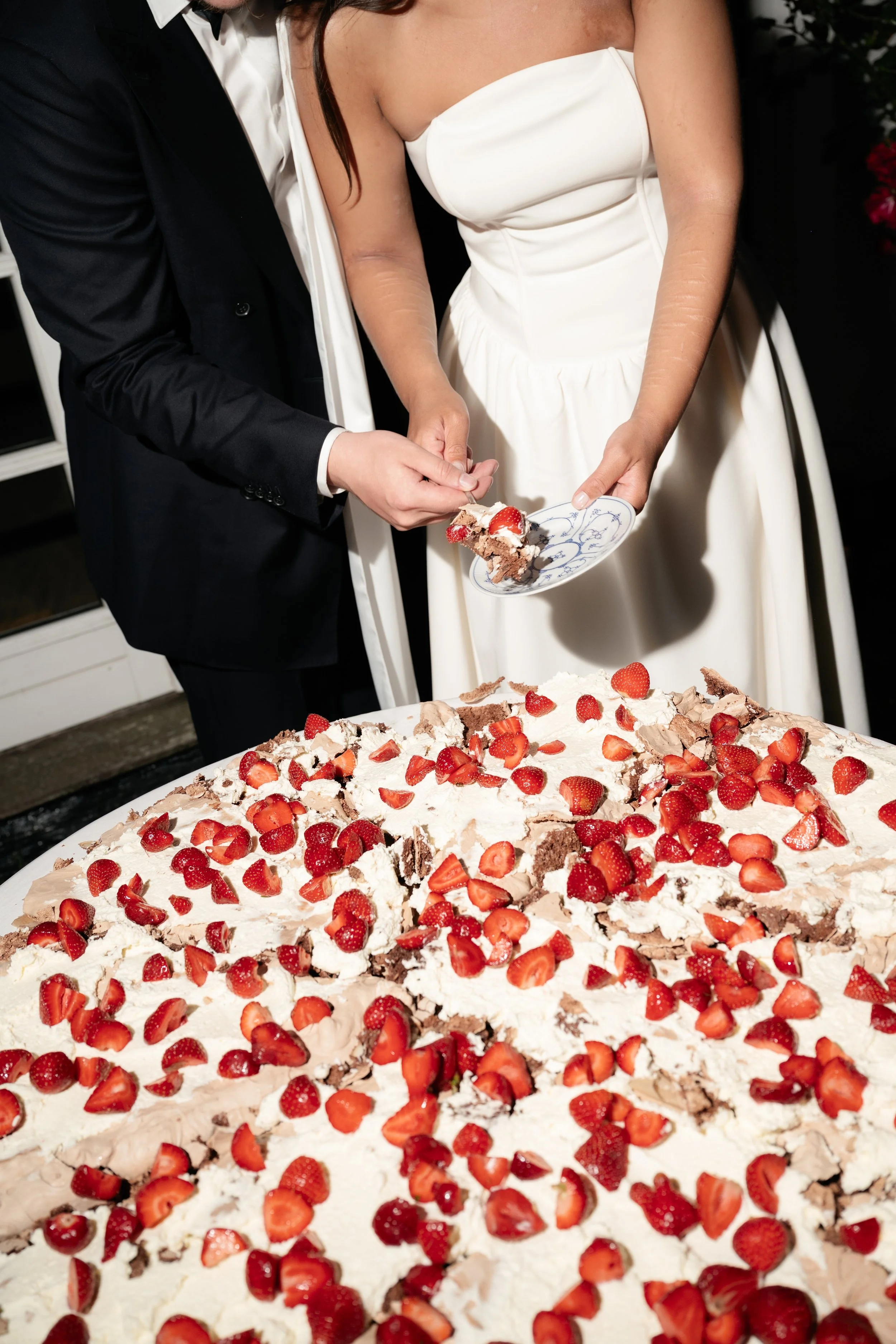 Bride and groom cutting and serving a large, decorated strawberry dessert cake at their wedding.