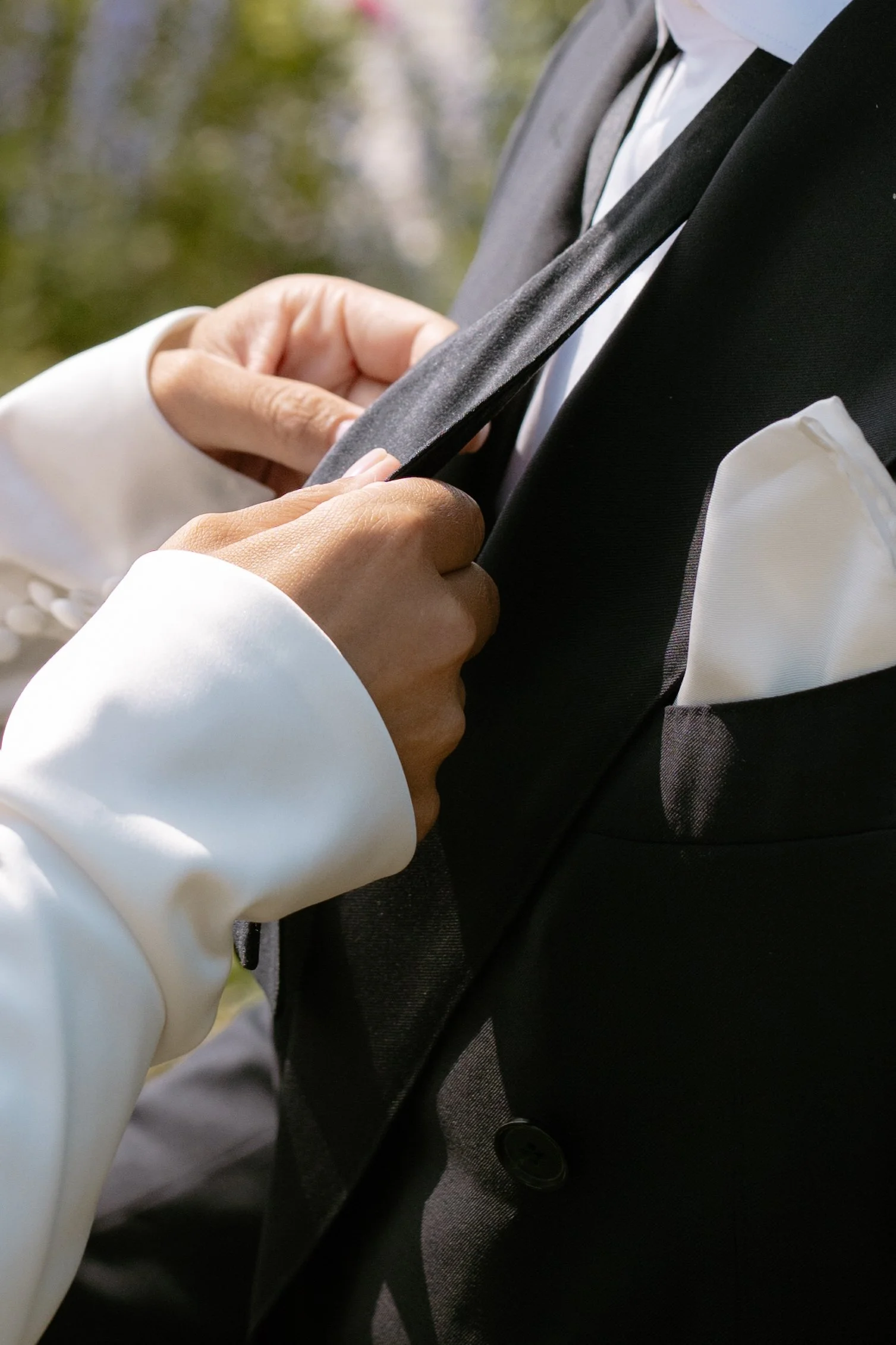 Person adjusts their black tuxedo jacket with a white shirt underneath, outdoors.
