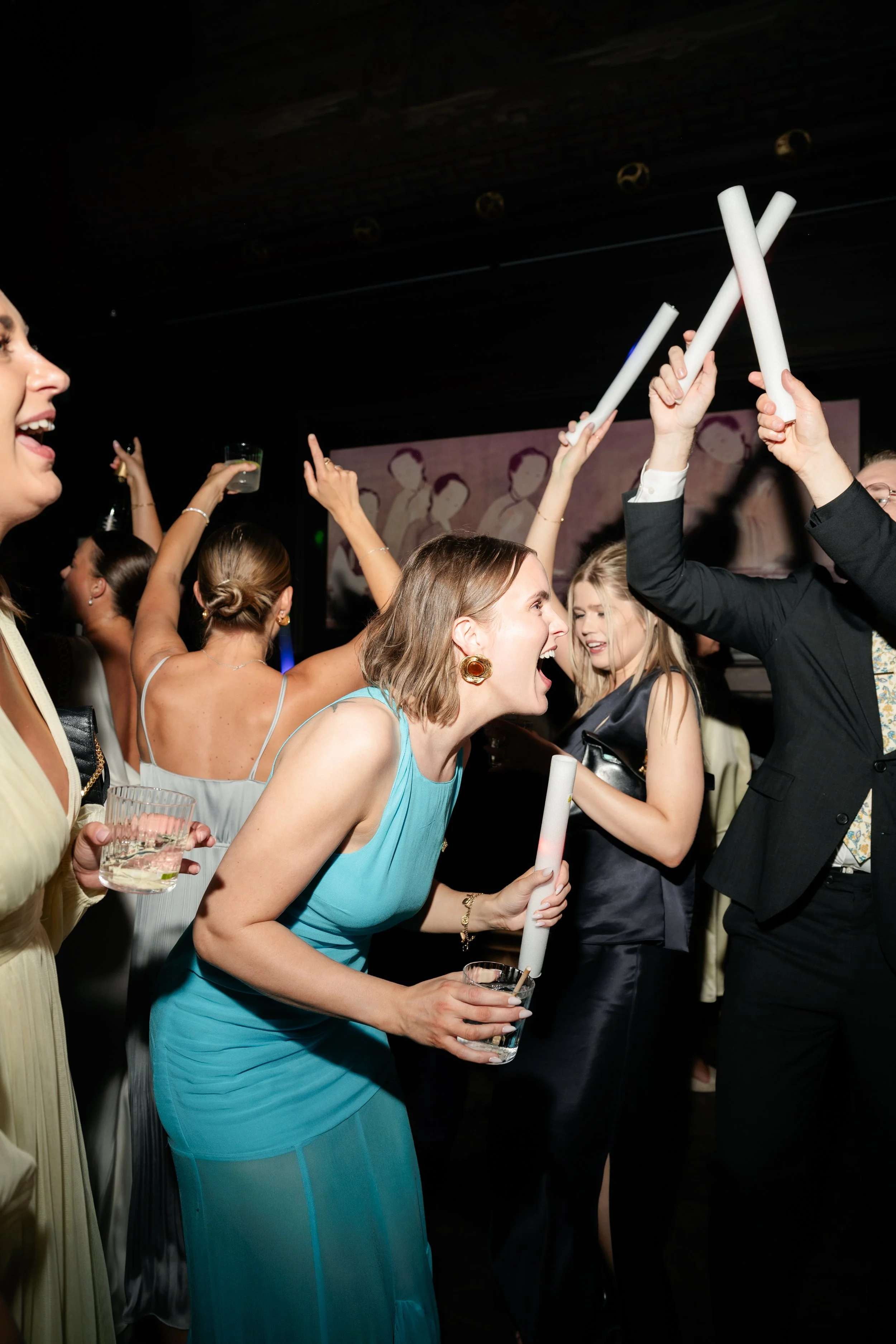 People celebrating at a party, holding drinks and glow sticks, dancing and having fun.