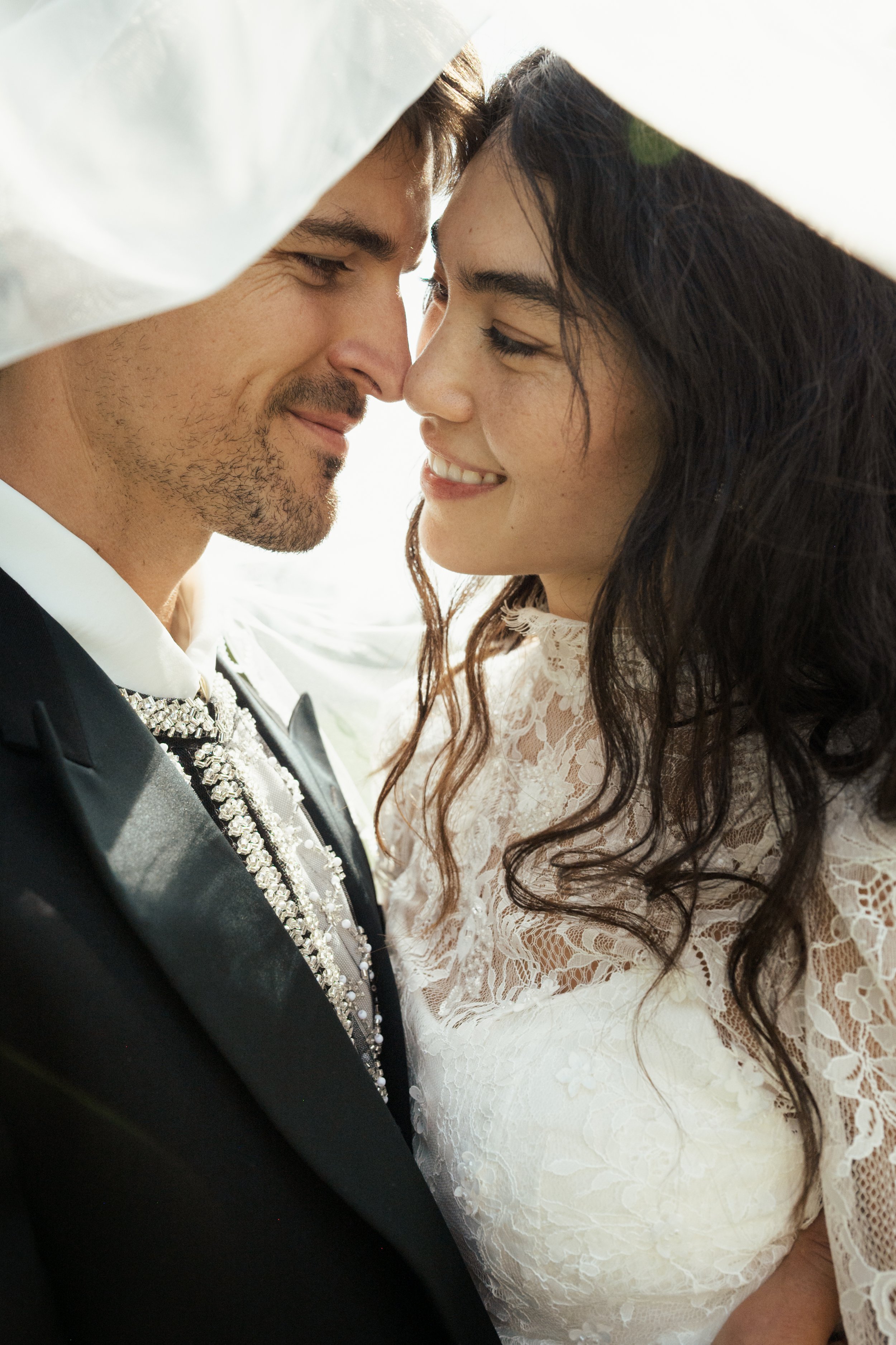 A couple dressed in wedding attire sharing a close, intimate moment, with foreheads touching and smiling.