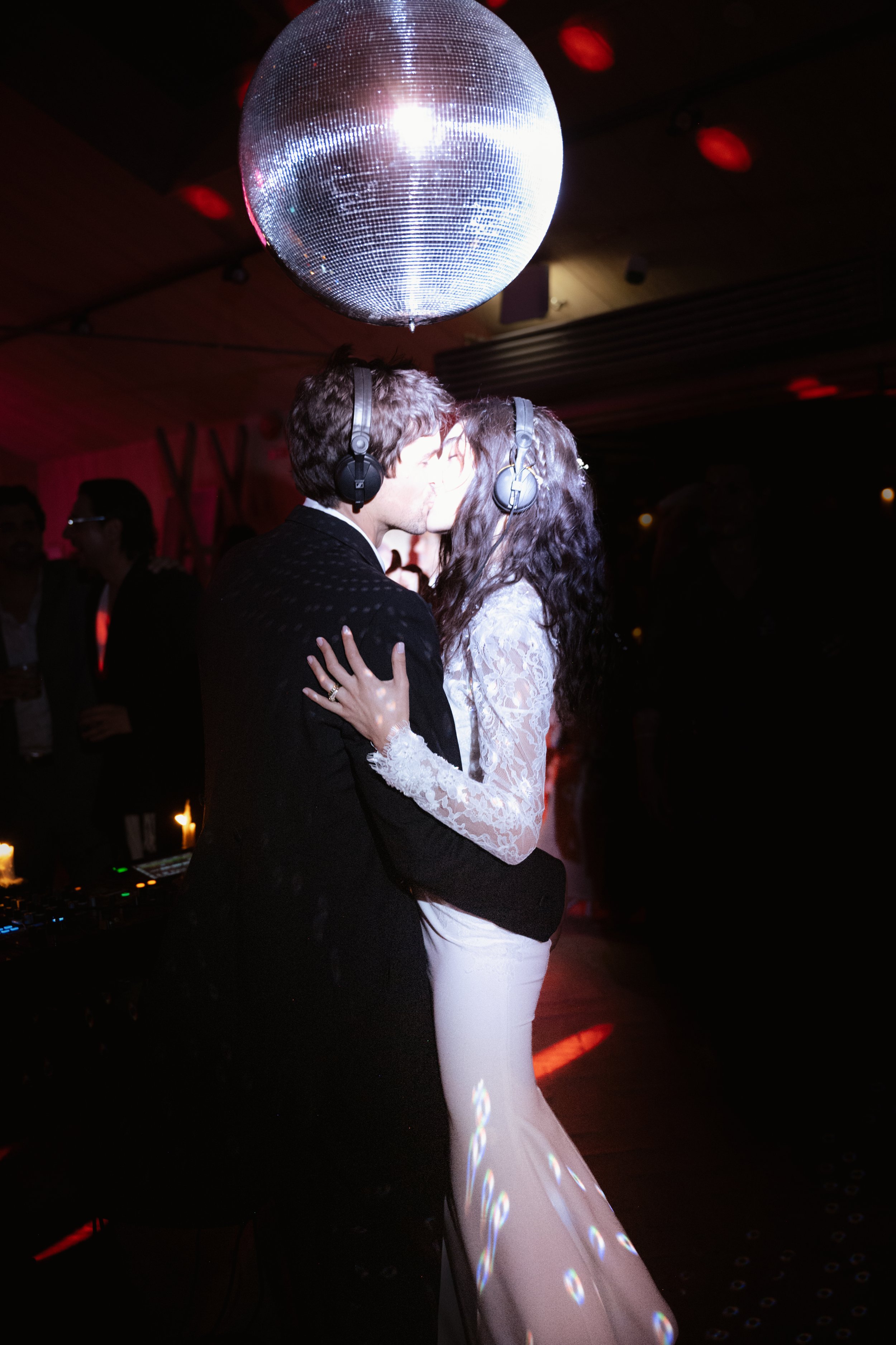 A couple dance and kiss on a dance floor under a disco ball at a party.