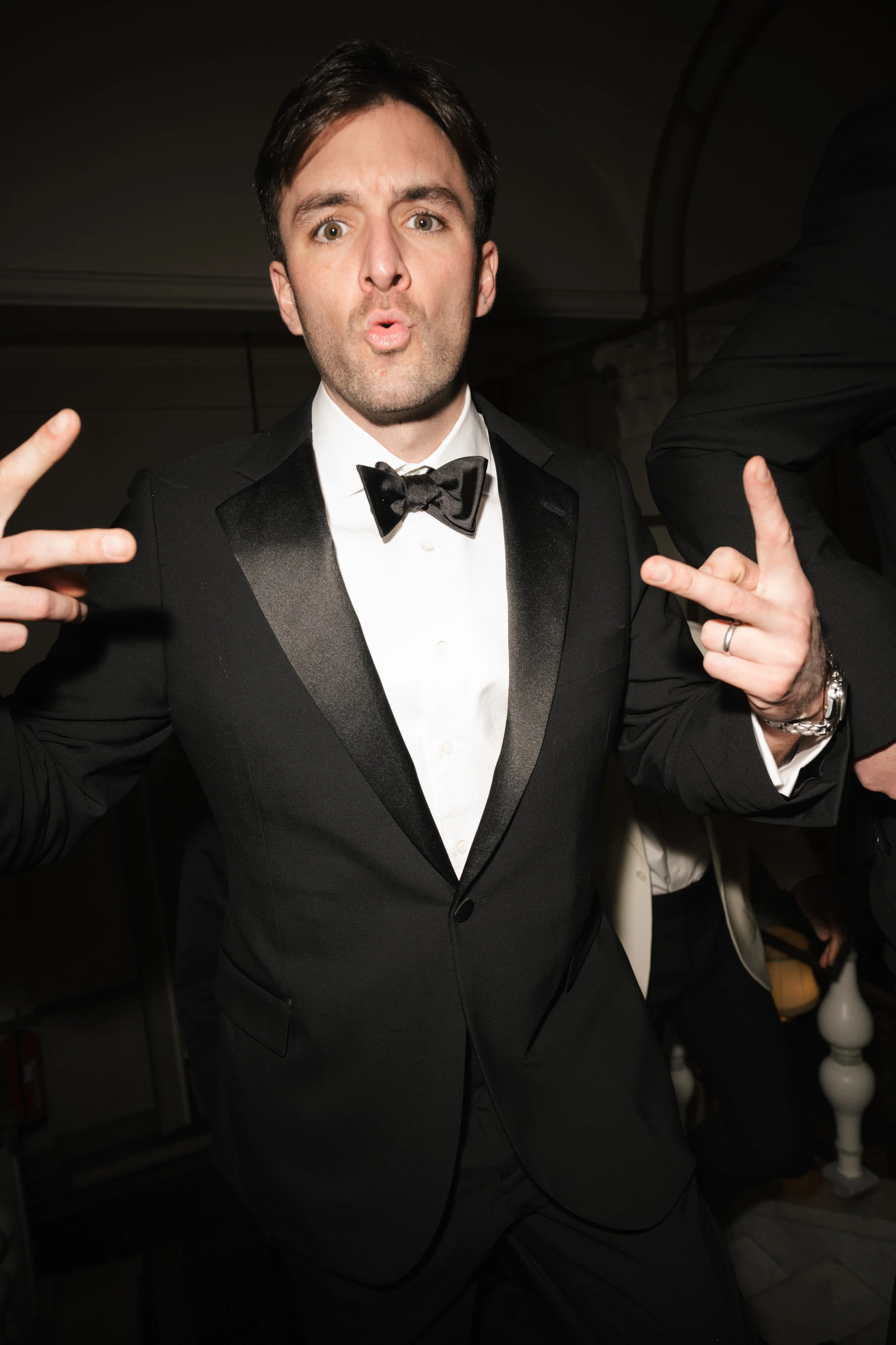 Man in a tuxedo making peace signs at a formal event.