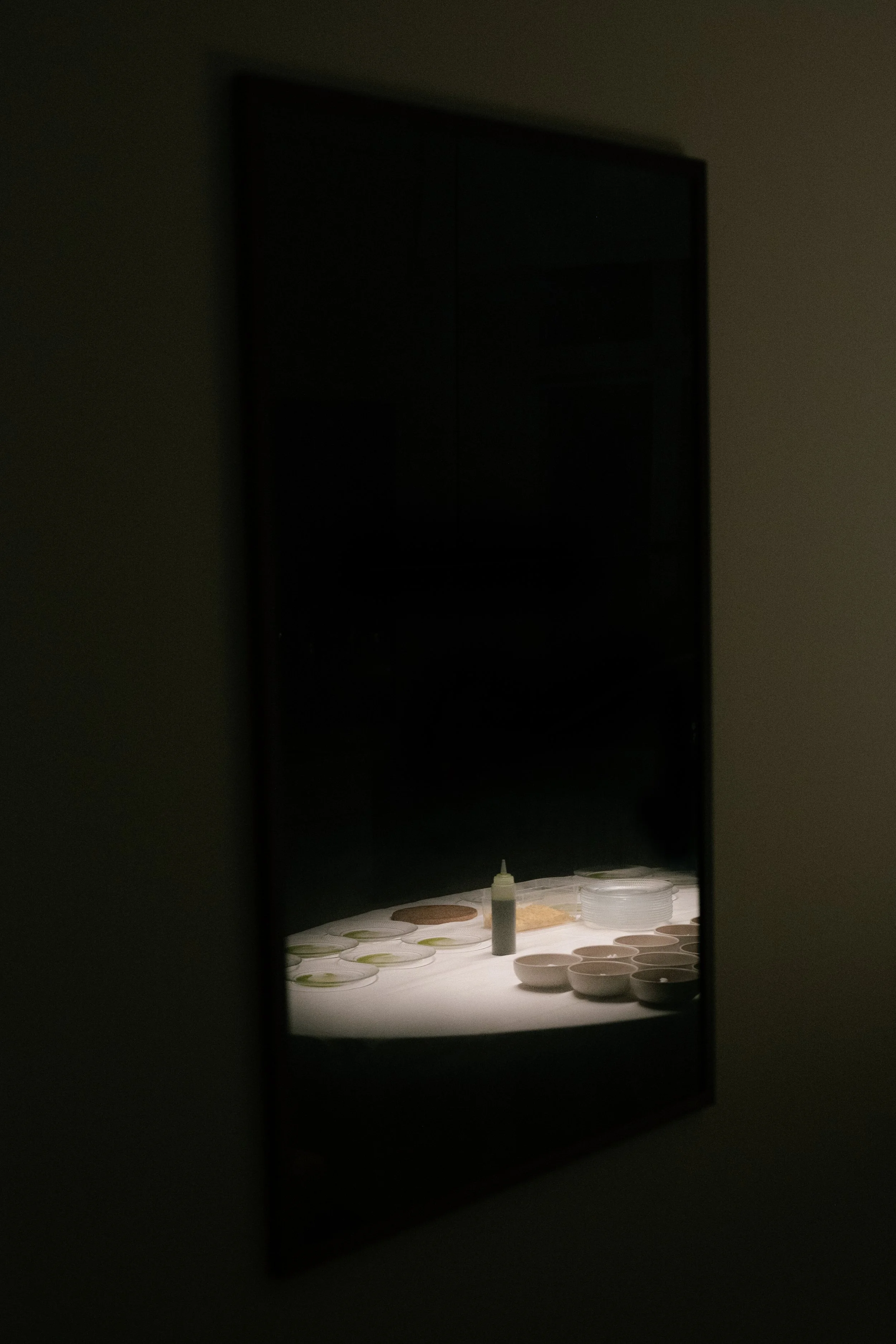 A dimly lit dining area with a table set with plates, bowls, and a bottle of sauce, seen through a mirror.