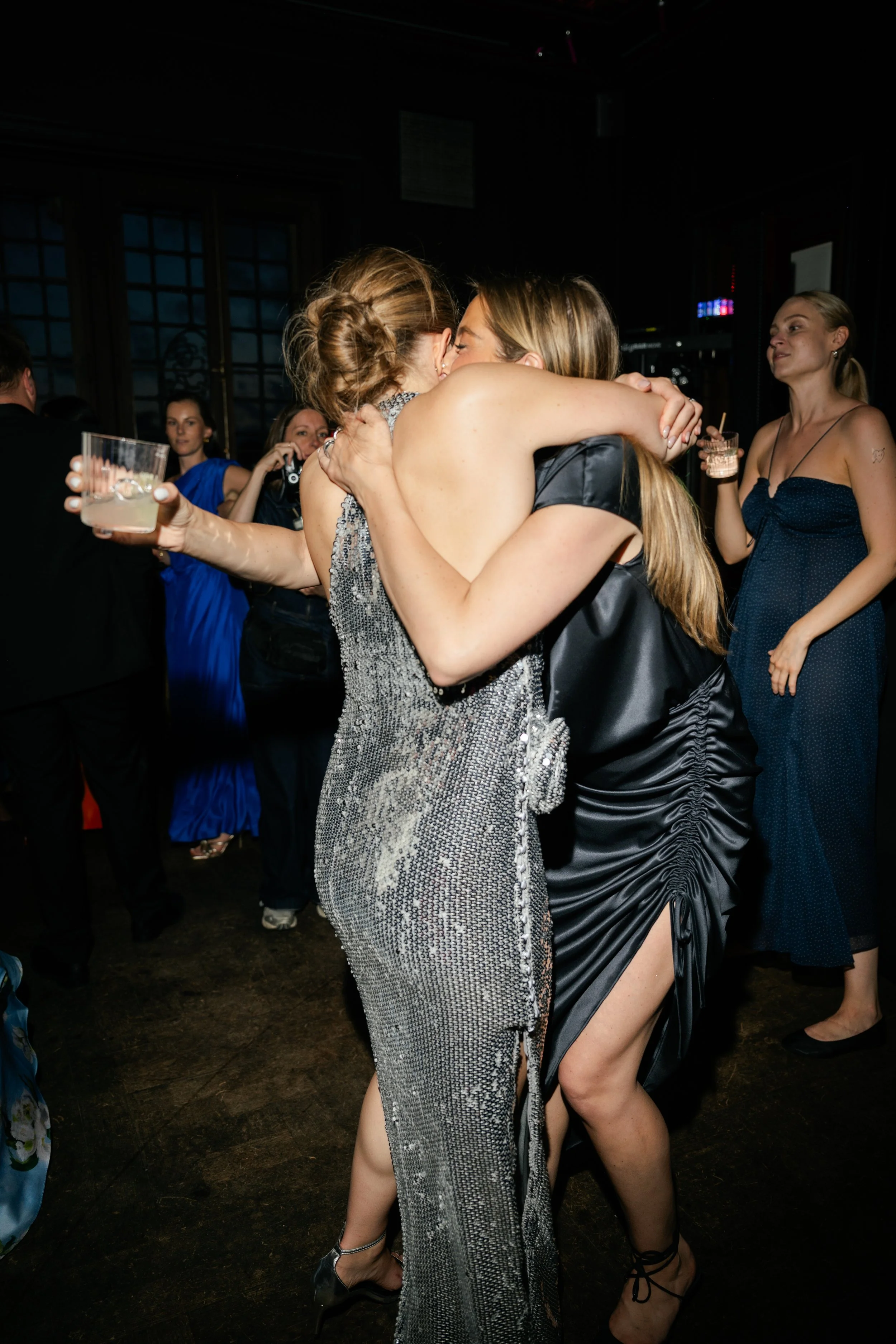 Two women hugging at a party, surrounded by other guests.