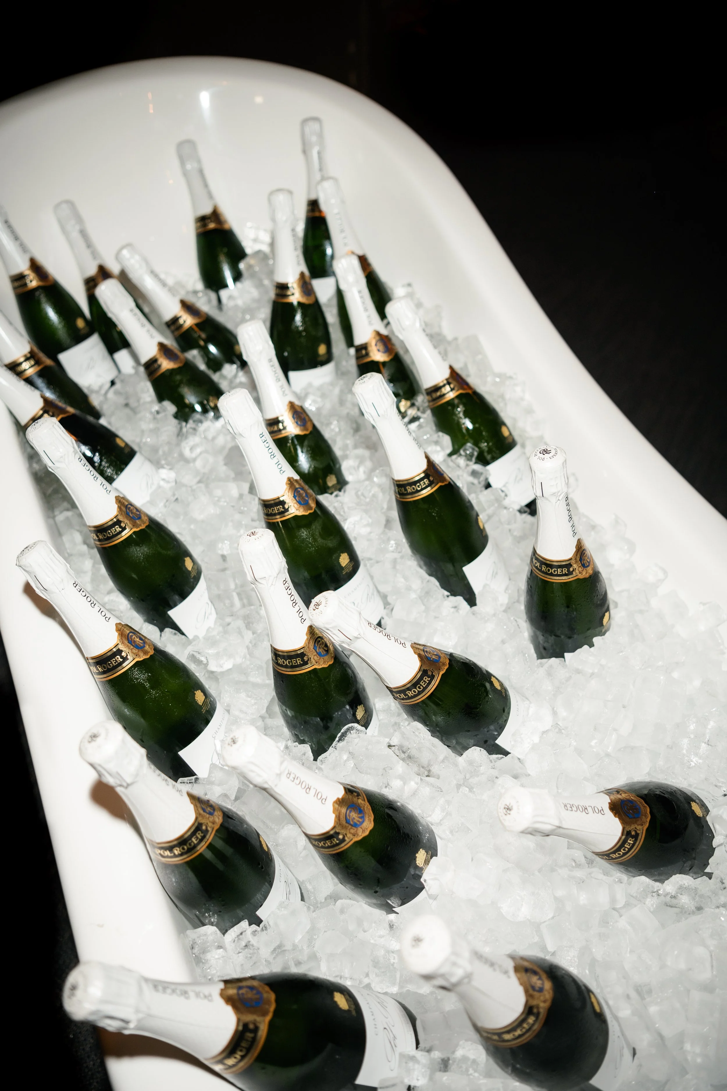 Multiple bottles of sparkling wine in a white cooler filled with ice.