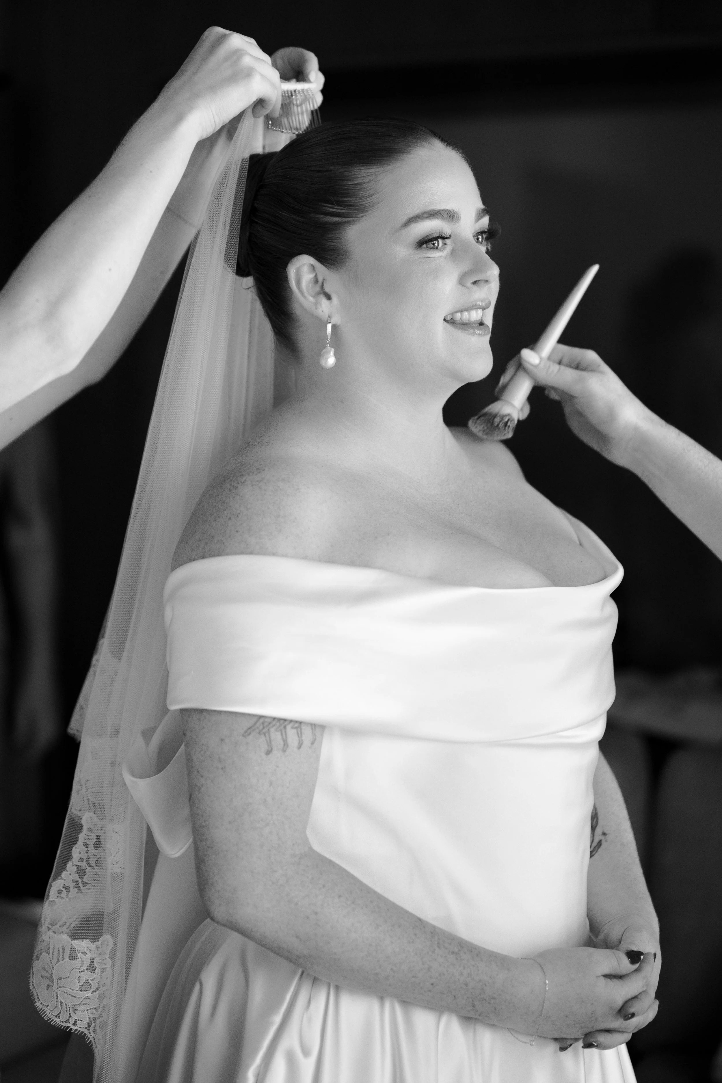 A bride getting her makeup finished while wearing a wedding dress and veil.