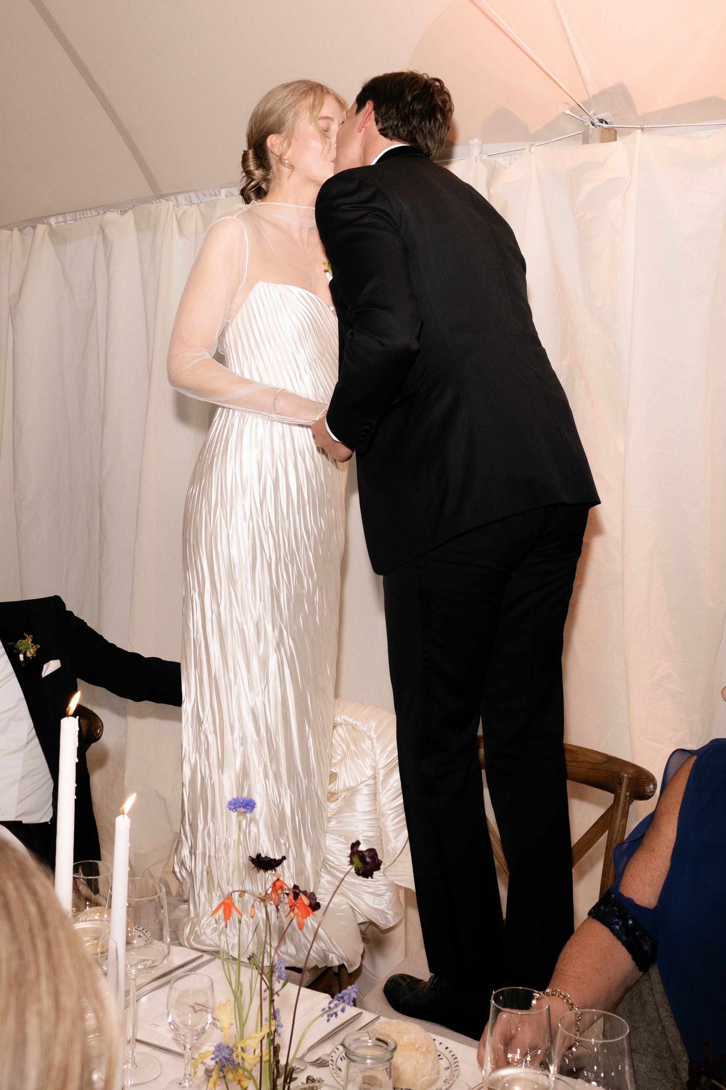 A bride and groom kissing on a wedding table during their wedding reception.