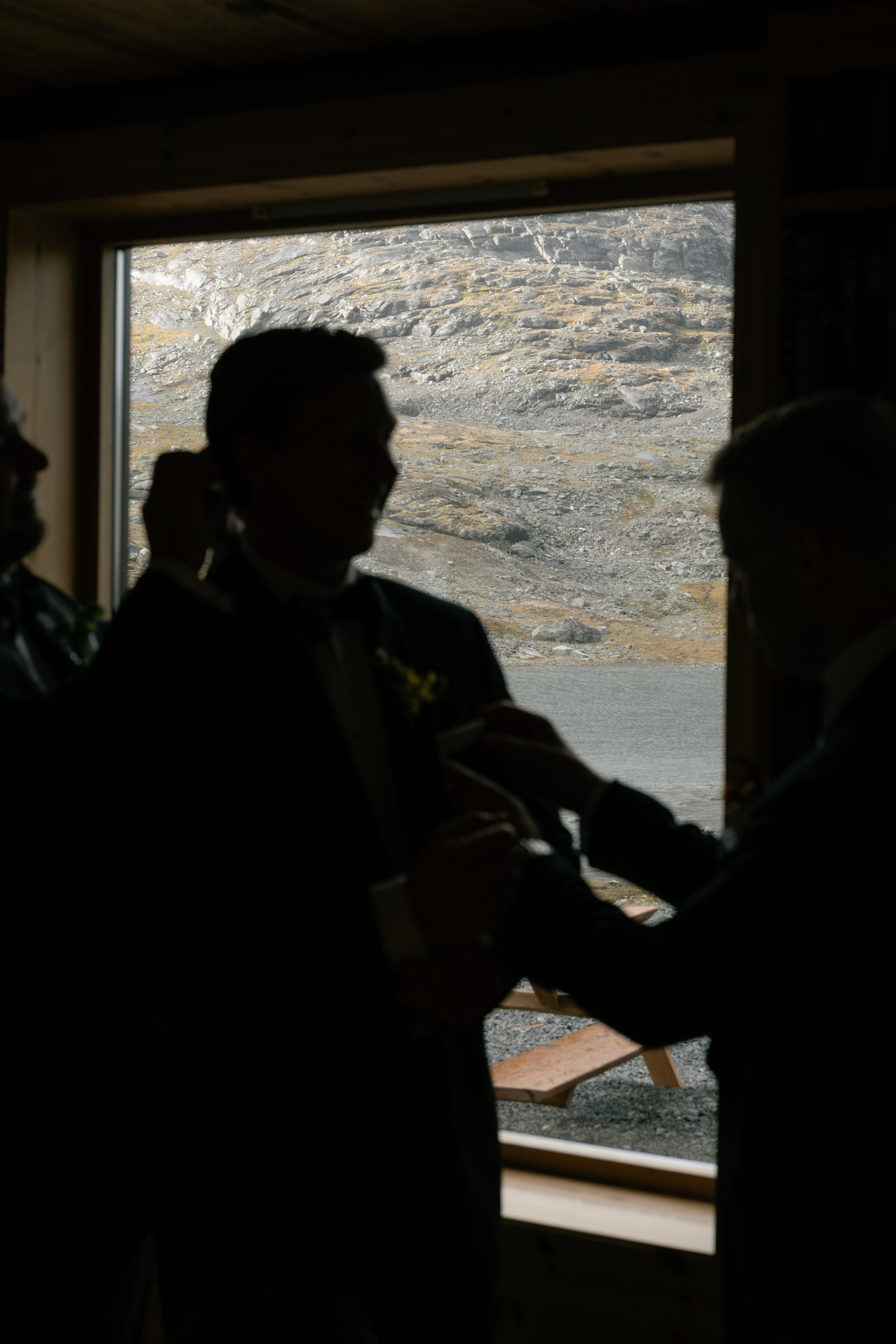 Silhouetted people inside a room with a window showing rocky mountainous terrain outside.