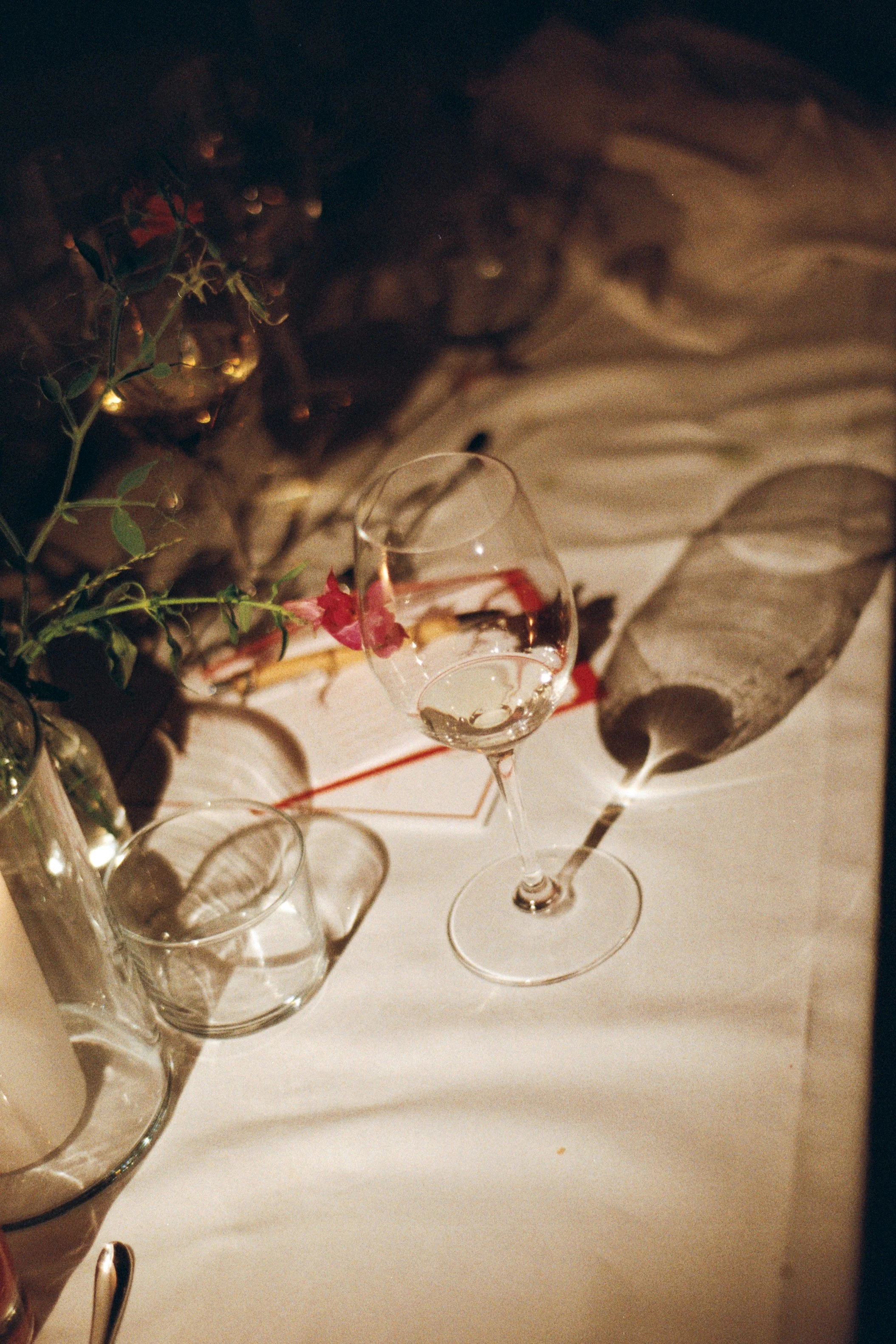 Elegant table setting with a wine glass, empty glass, decorative leaves, and a wax candle on a white tablecloth.