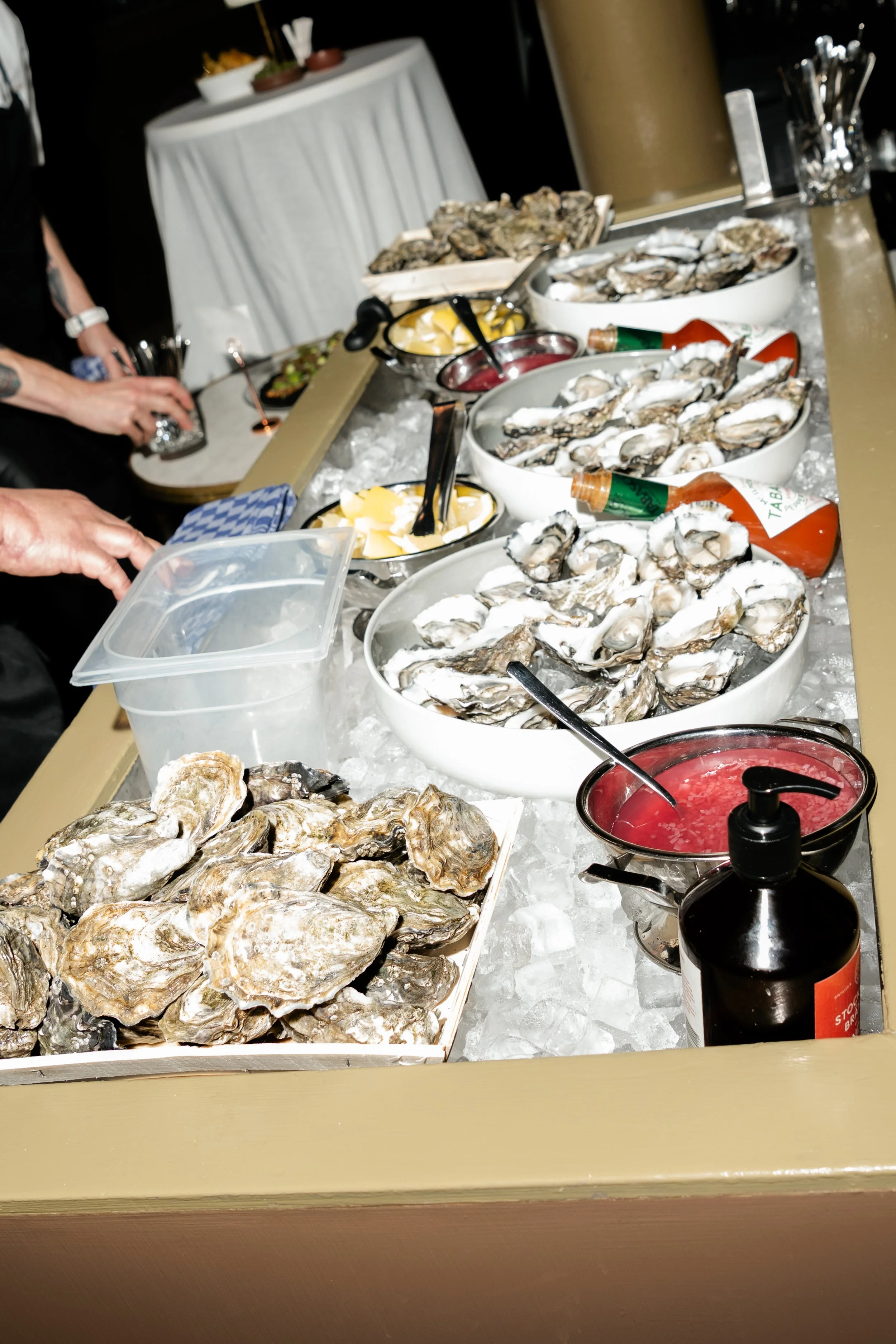 A seafood buffet with ice, oysters, lemon wedges, cocktail sauce, and condiments.