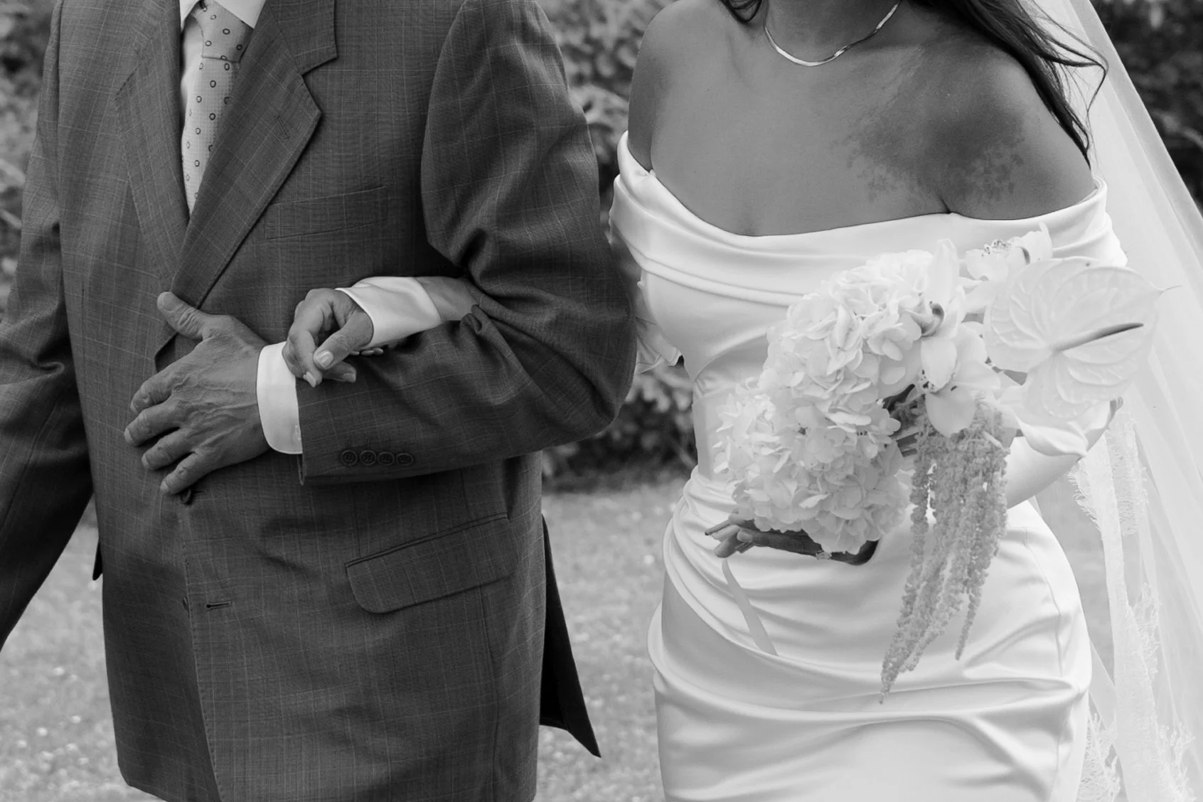A bride in a wedding gown holding a bouquet of flowers, walking arm-in-arm with a man in a suit at a wedding ceremony.