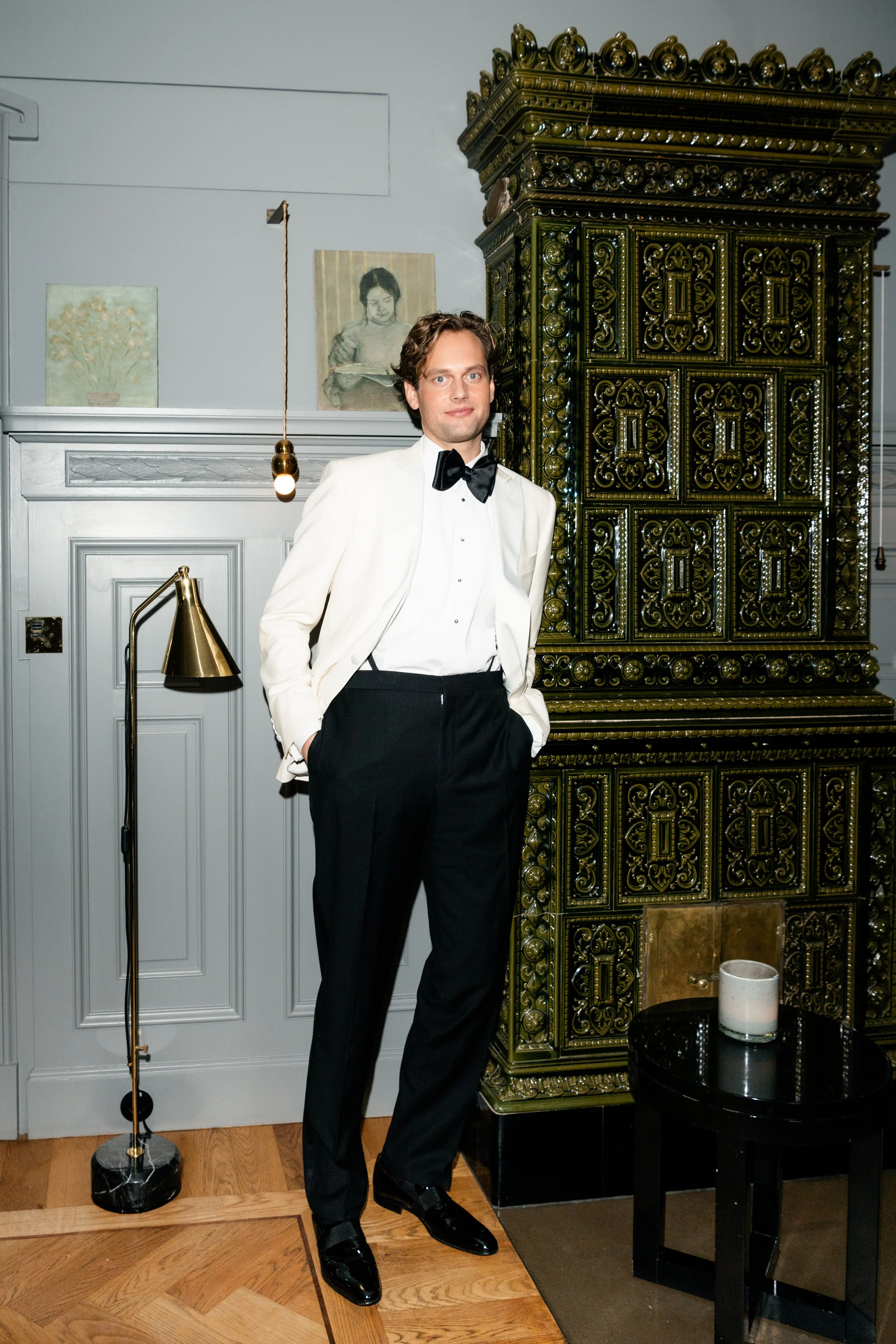 A man in a tuxedo and white blazer standing in a decorated room.