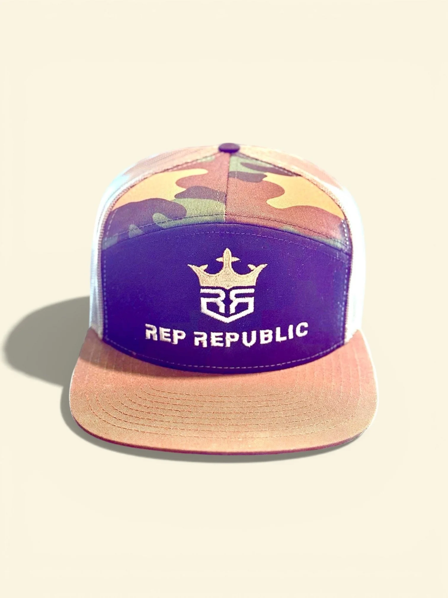 A baseball cap with a camouflage pattern, a purple front panel featuring a crown logo, and the words "REPUBLIC" embroidered below.