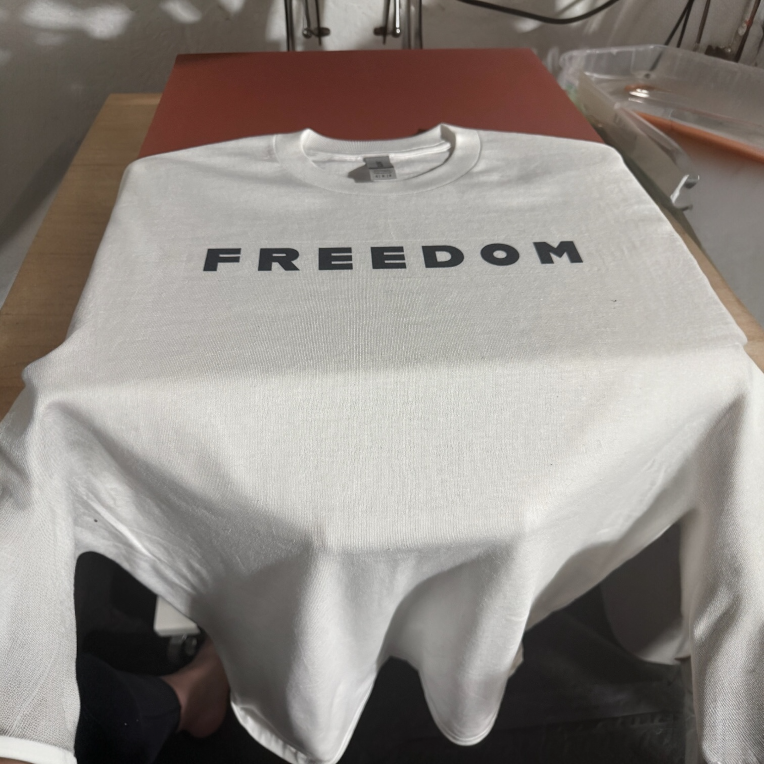 White T-shirt with the word 'FREEDOM' printed in black, laid flat on a table.