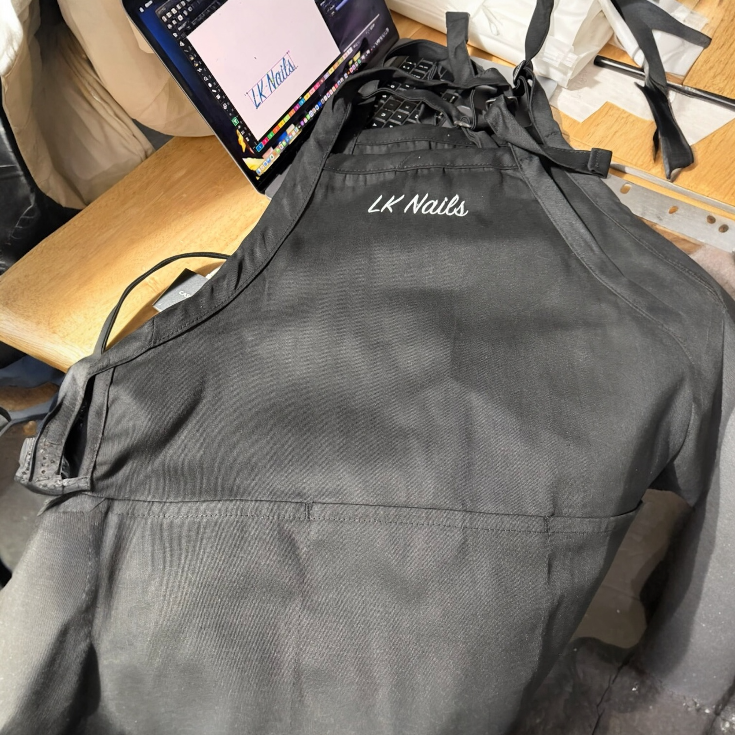 A black garment bag with 'LK Nails' embroidered on it, placed on a table near a laptop and a box of business cards.