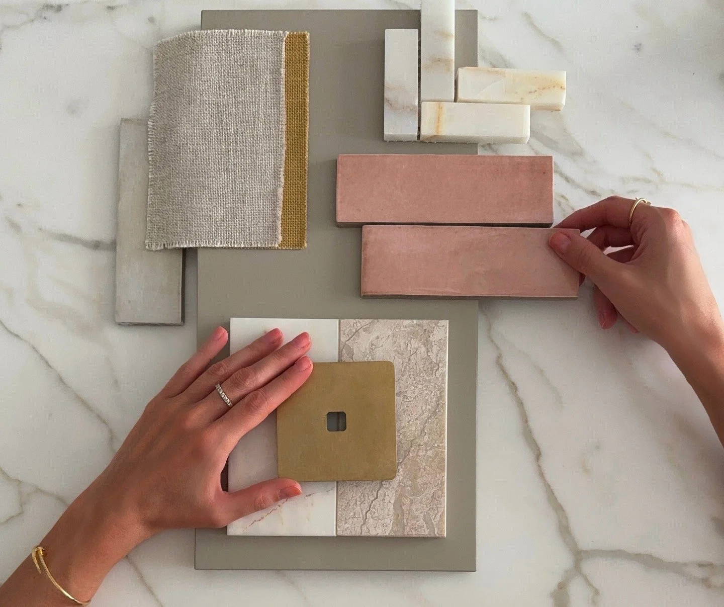 Hands arranging and selecting material samples including tiles, stones, and fabric swatches on a marble surface for interior design or renovation.