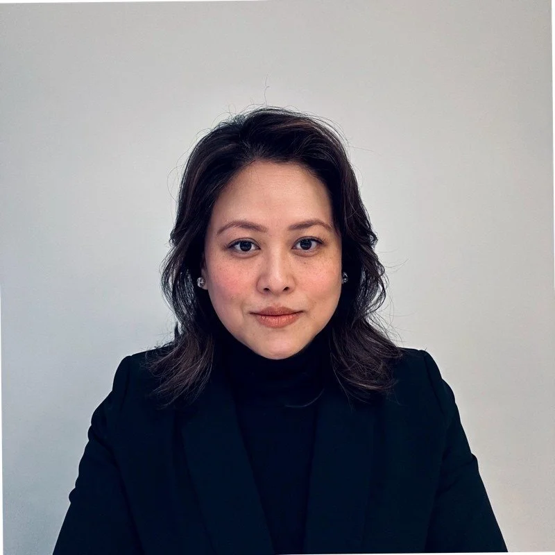 Head shot of woman with dark hair, who is wearing black turtleneck against white background.