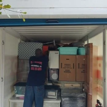 A man packing or unpacking items into a storage unit with boxes and household items.