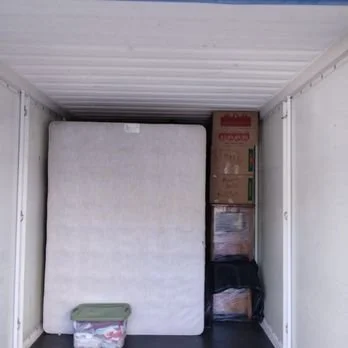 Interior of a storage container with boxes and a mattress.