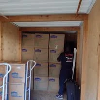 Person organizing boxes in a storage unit with wooden walls and ceiling.