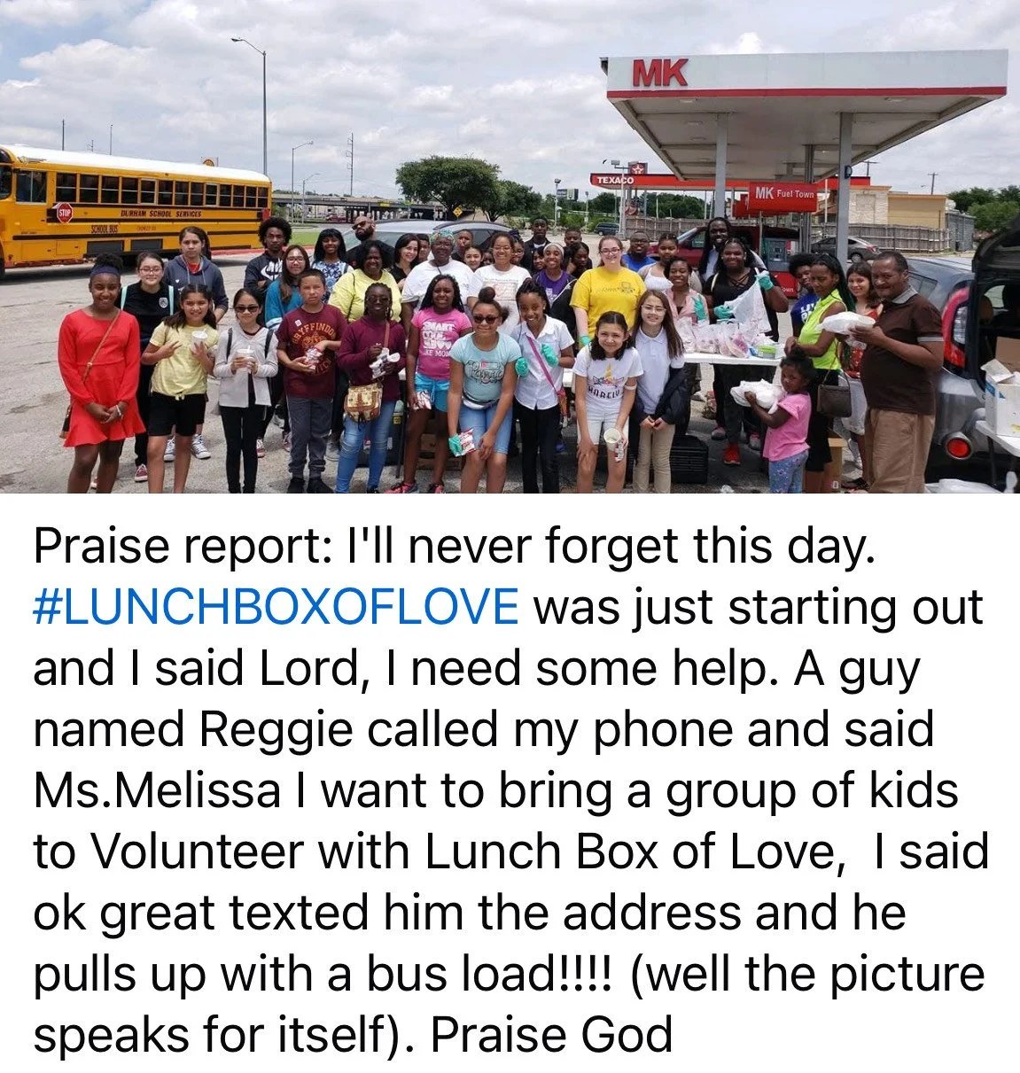 A large group of kids and adults gathered in a parking lot beside a food truck and a school bus, with many smiling at the camera. The scene shows an outdoor setting with cloudy skies.