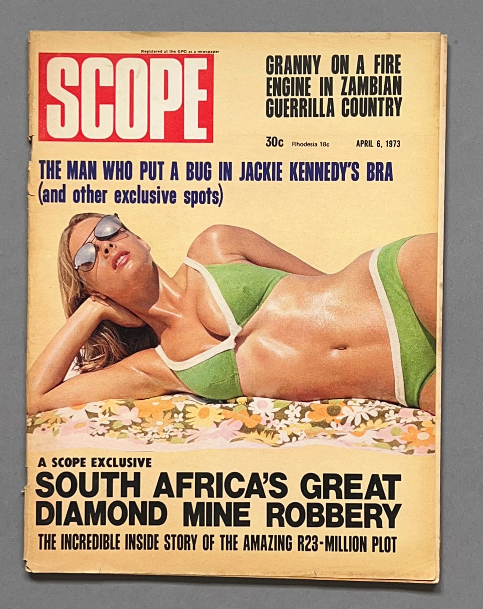 Vintage magazine cover featuring a woman in a green bikini lying on a floral surface, with the headline about South Africa's diamond mine robbery.
