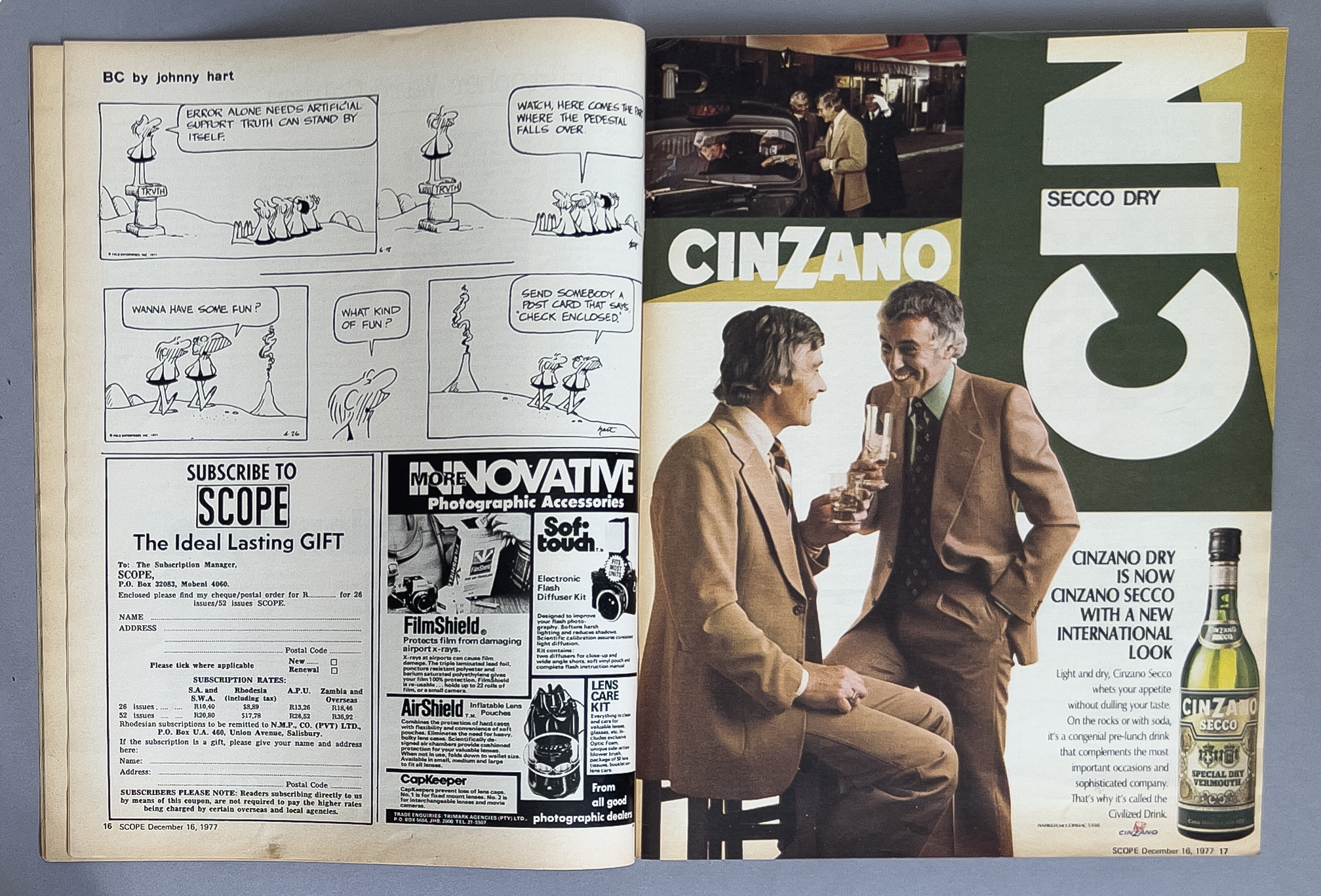 Magazine spread featuring a vintage comic strip, advertisements, and a large photo of two men in suits clinking glasses. The comic strip tells a humorous story about a pedestal, with speech bubbles, and the ads promote photographic accessories and a 