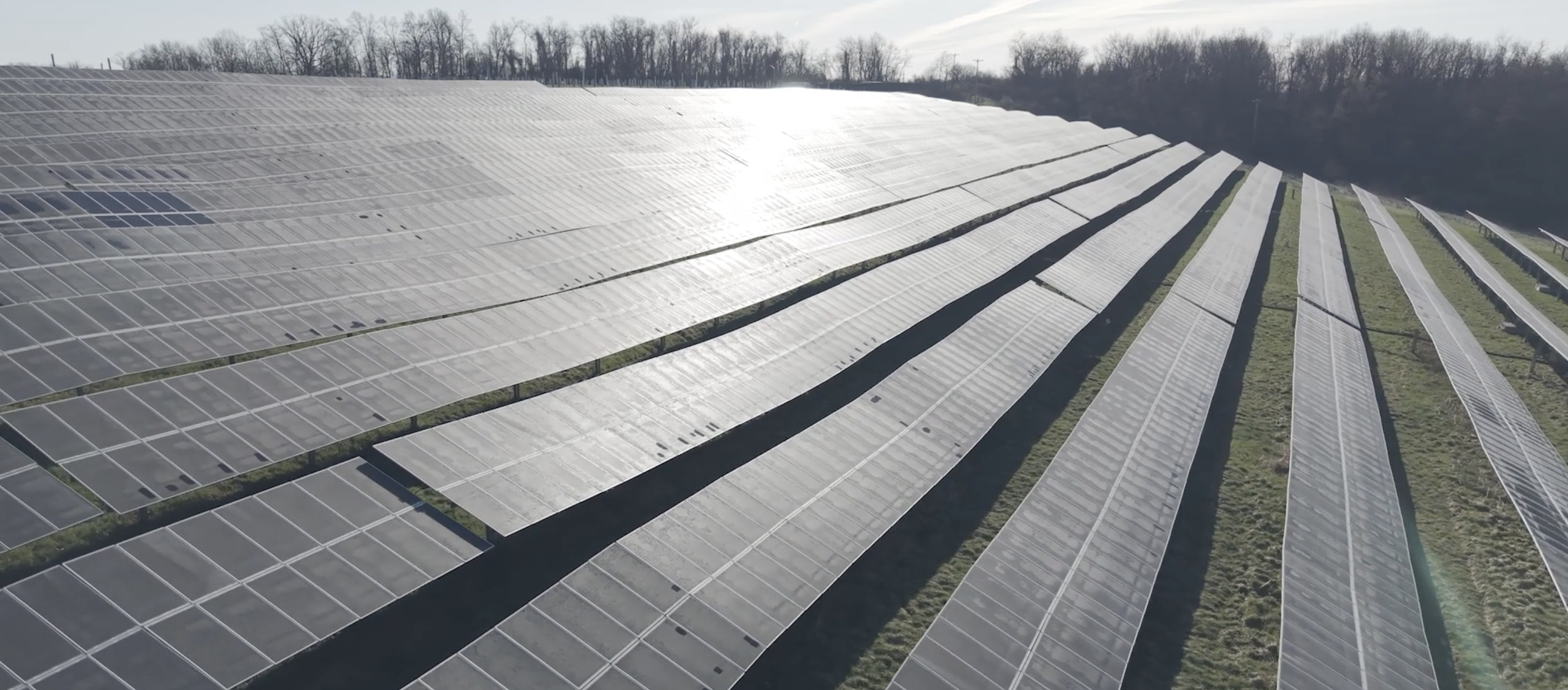 Solar panels installed on a grassy field with cloudy sky above.