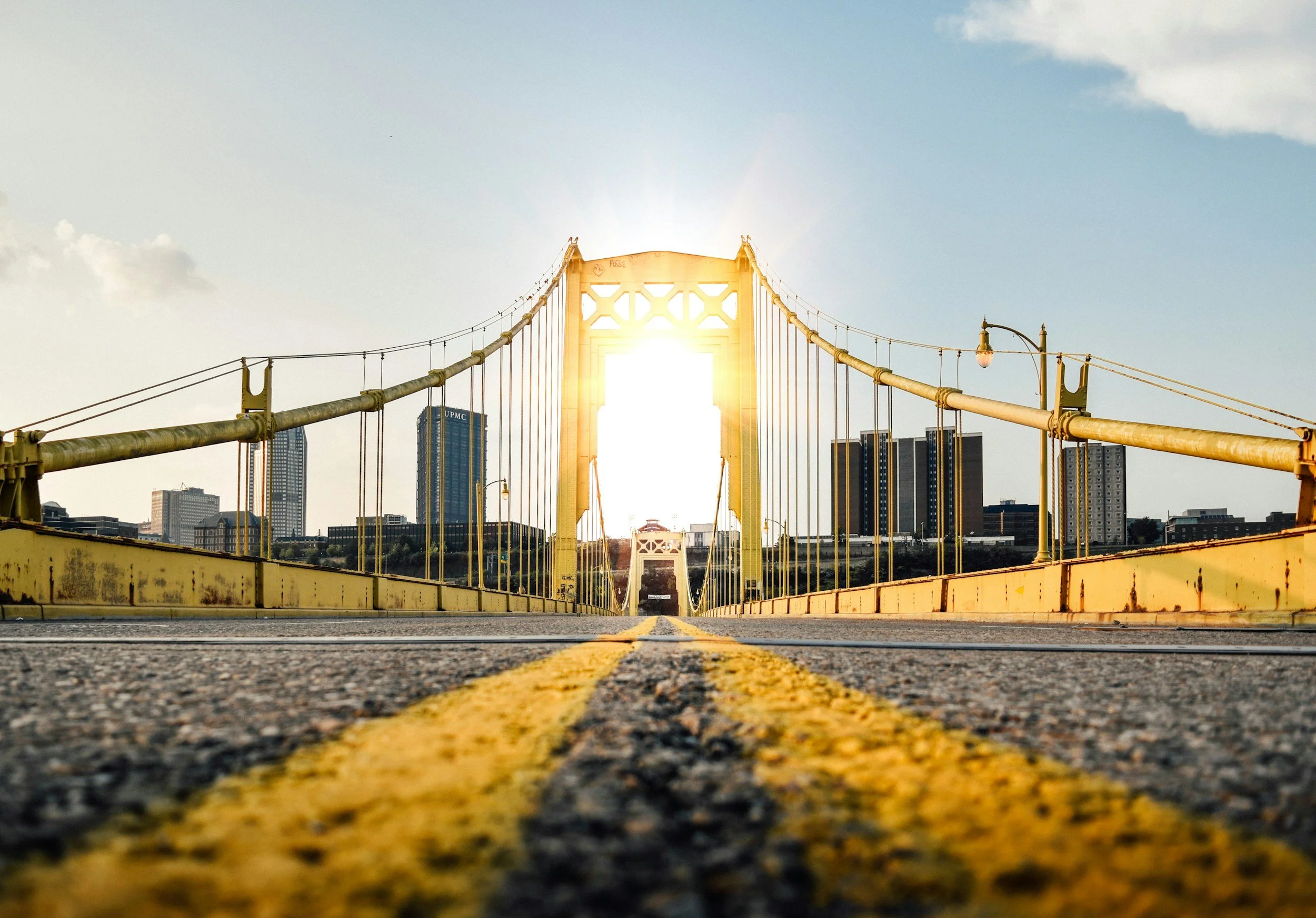 Low-angle view of a yellow suspension bridge with city skyline in background during sunset.