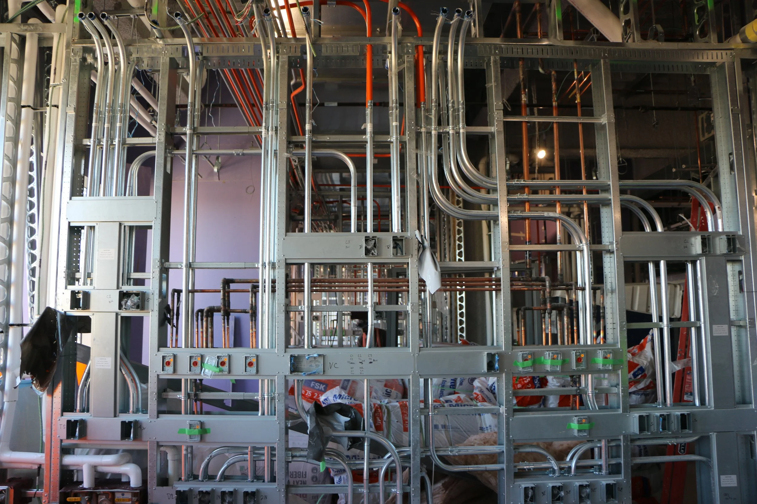 Framework of electrical and plumbing conduits being installed in a building interior under construction.