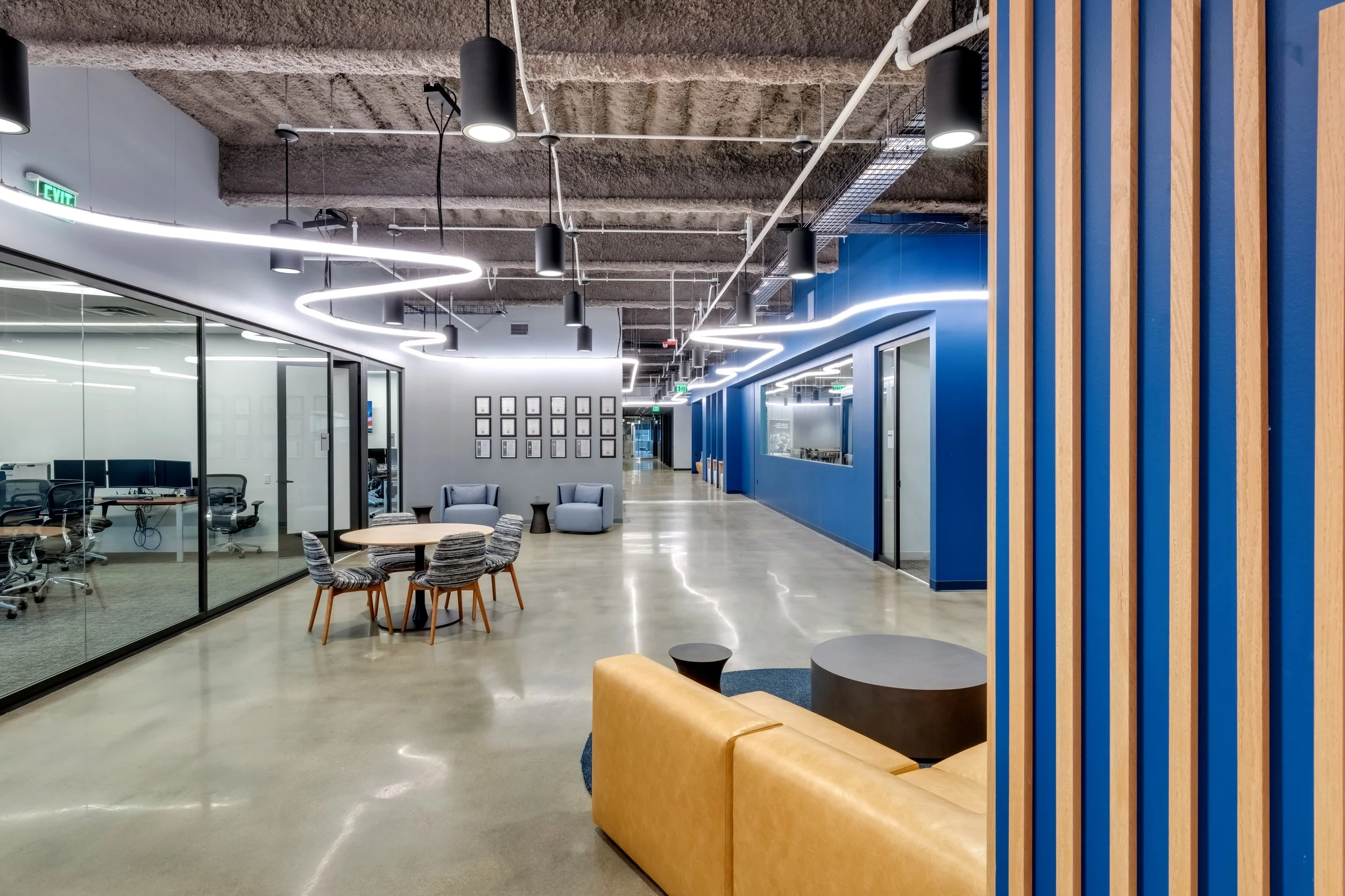Modern office lobby with seating area, blue accent wall, glass walls for meeting rooms, and contemporary lighting fixtures.
