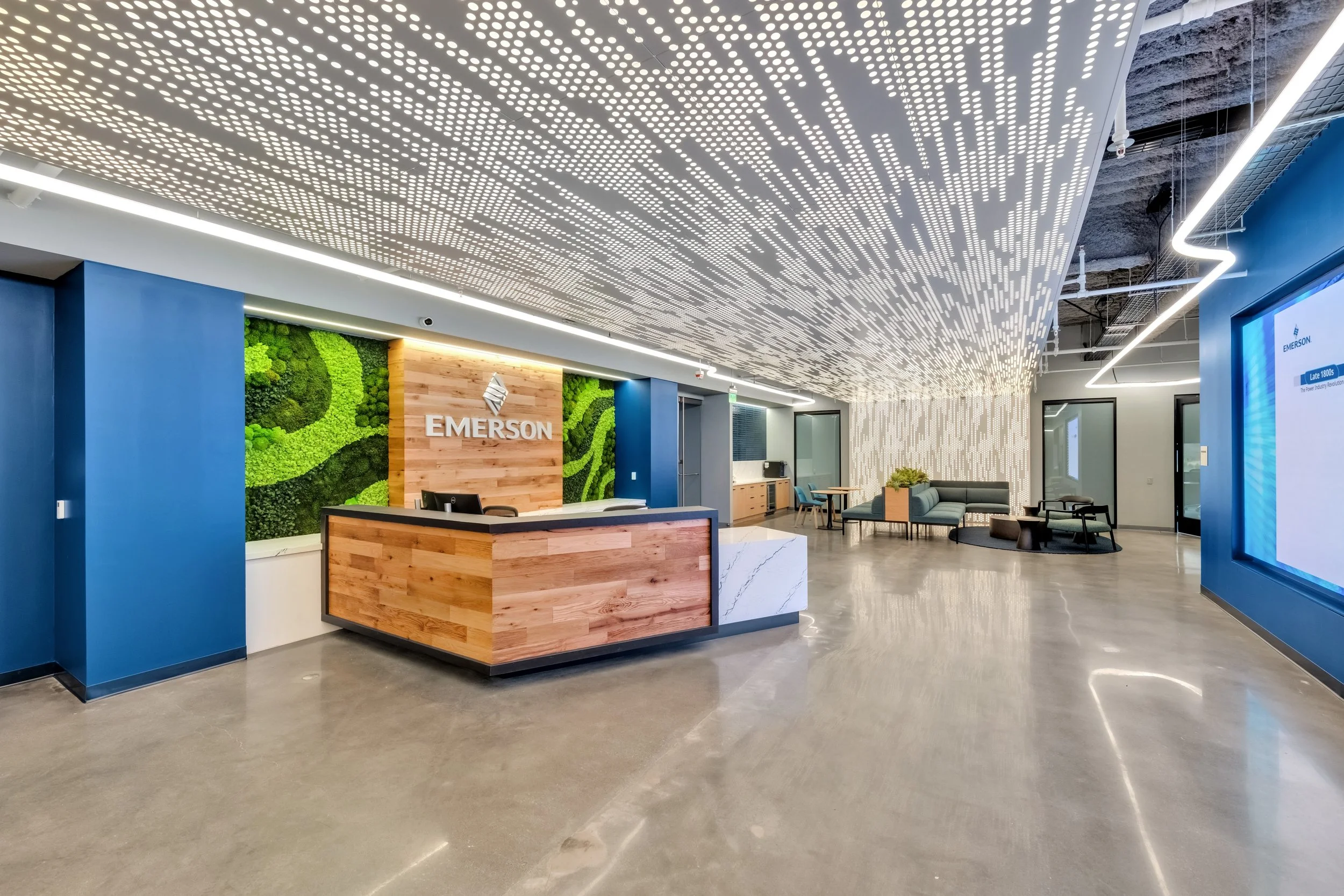 Modern office reception area with a wooden desk, green wall decor, comfortable seating, and an illuminated ceiling design.