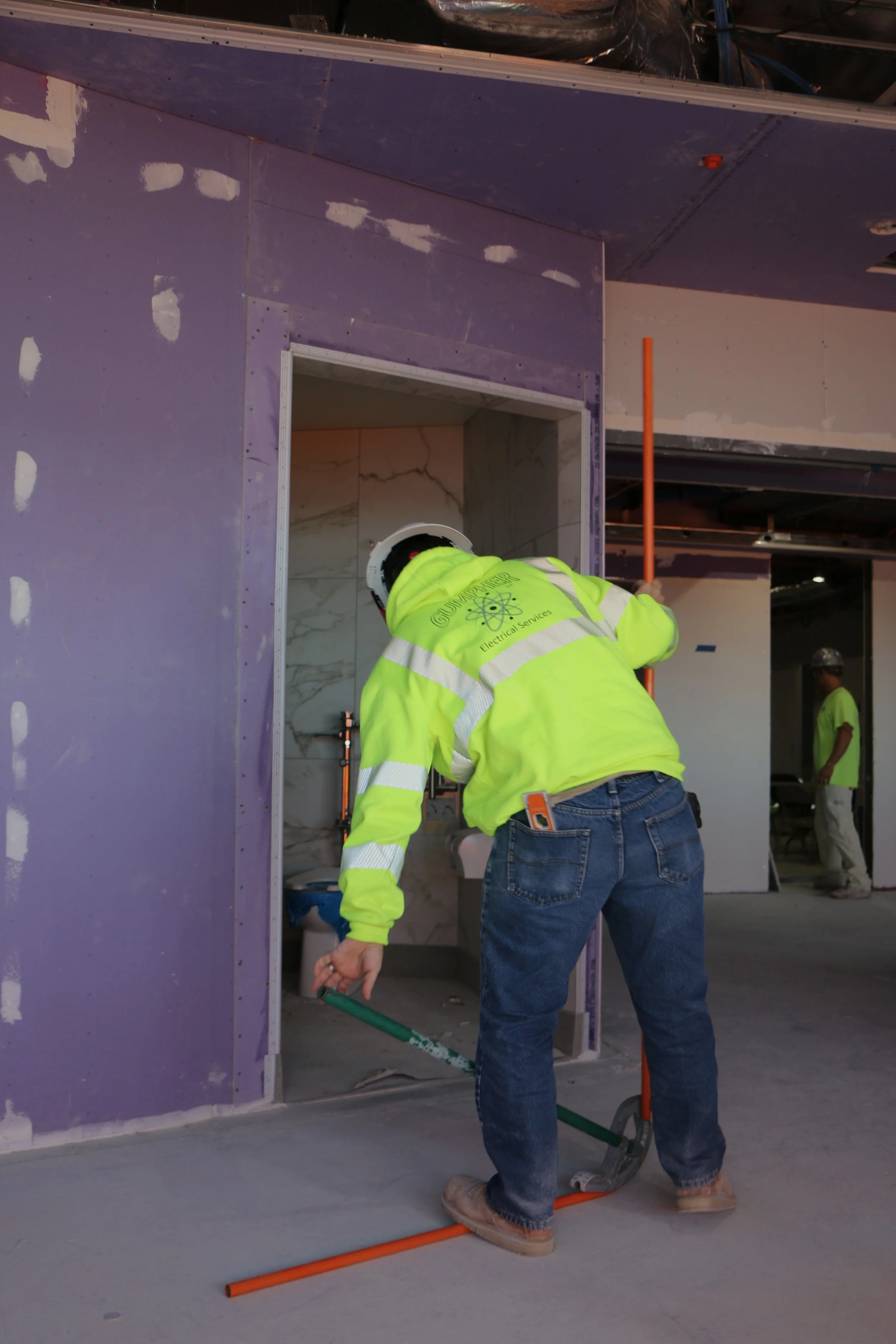 Electrician in a high-visibility jacket working on conduit piping in a building under construction.