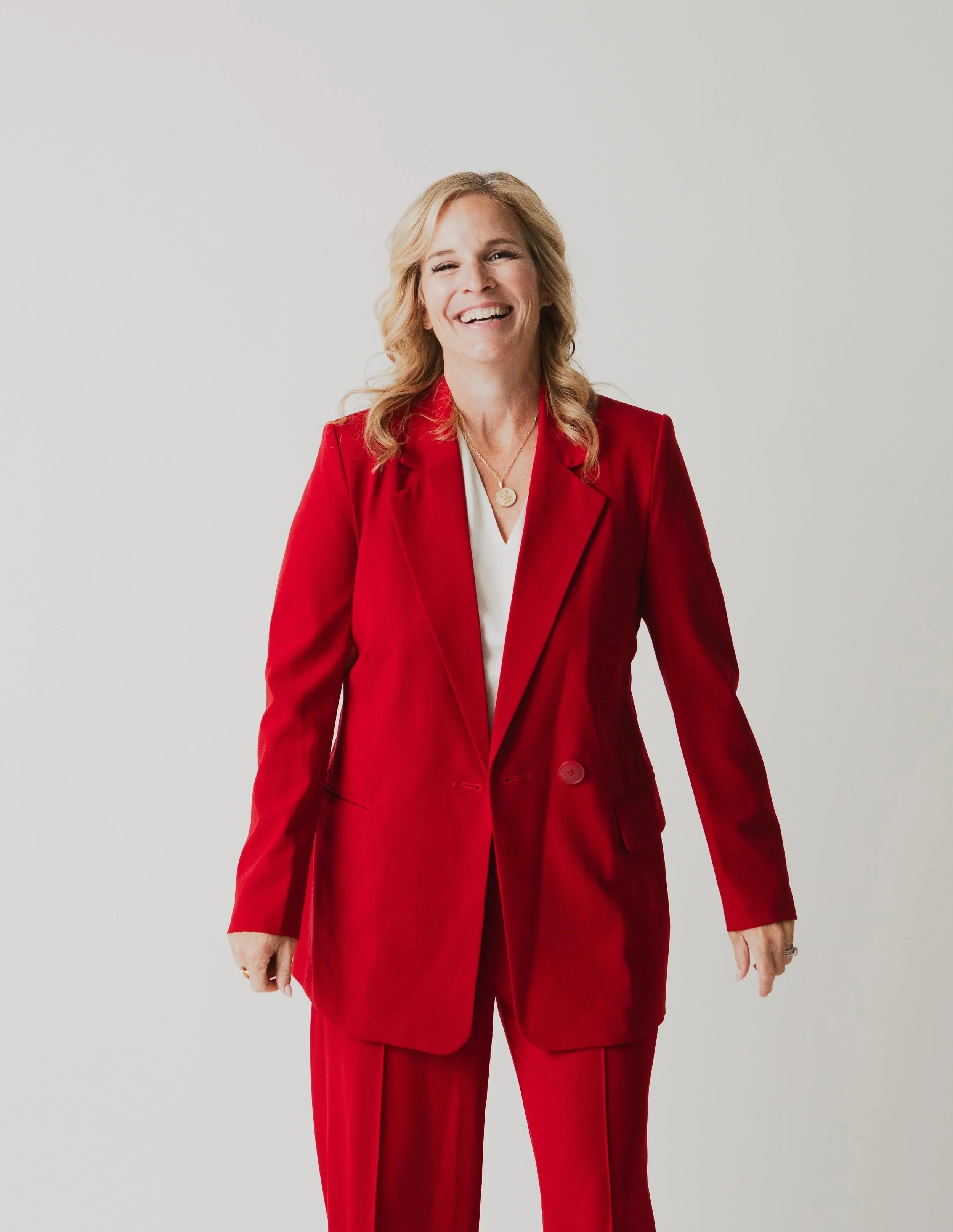 A woman wearing a red suit with a white blouse, smiling against a plain white background.
