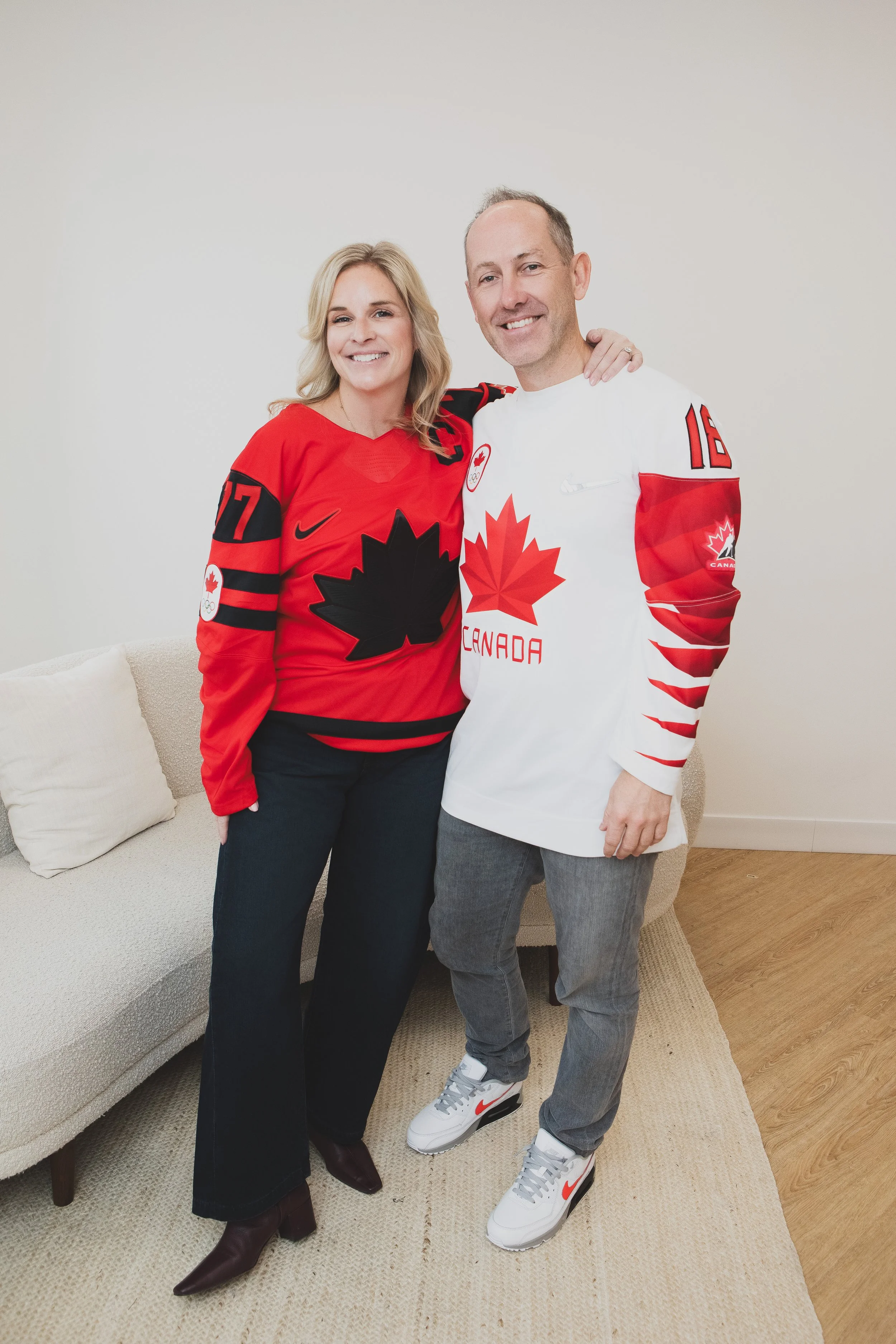 A man and woman standing together indoors, both wearing Canadian hockey jerseys, smiling at the camera.