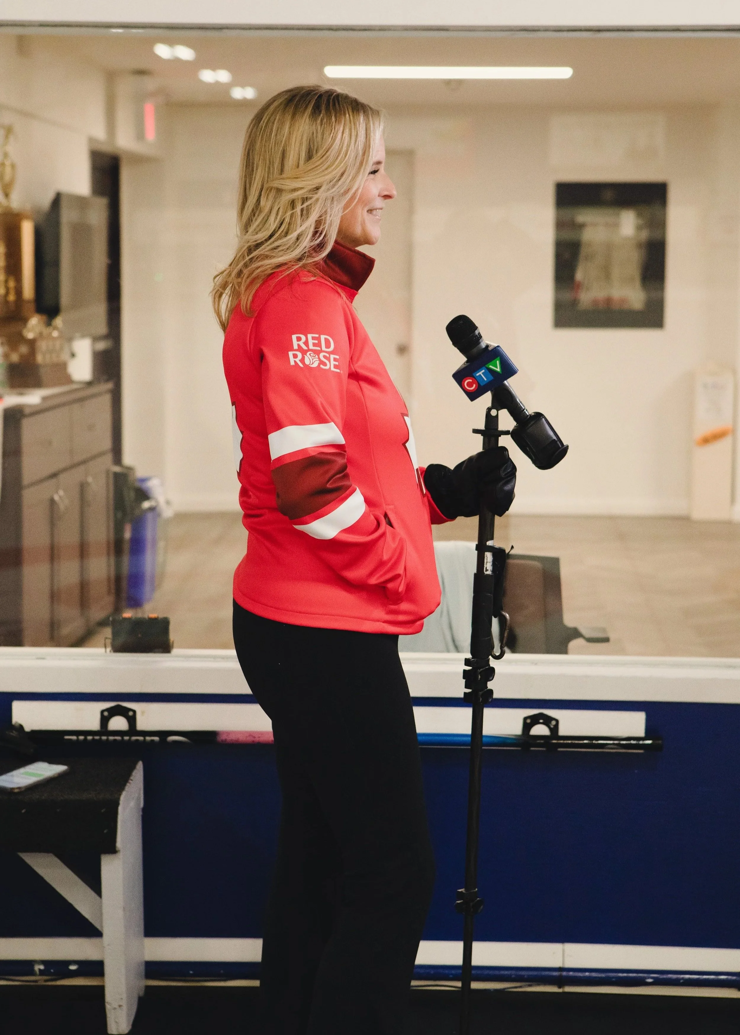 A woman in a red jacket holding a microphone with a CTV logo, standing indoors near a window.