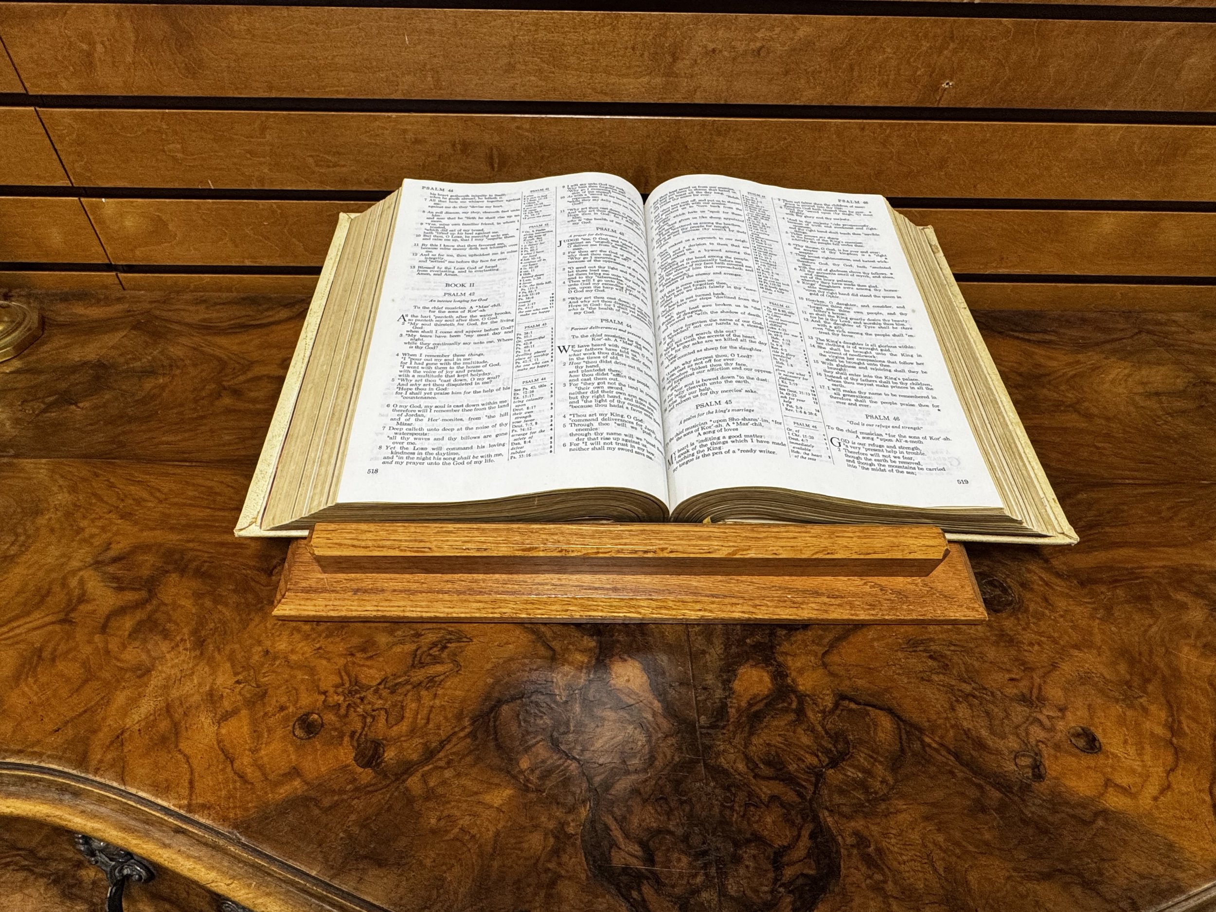 Open Bible resting on a wooden pulpit with a wood-paneled wall in the background.