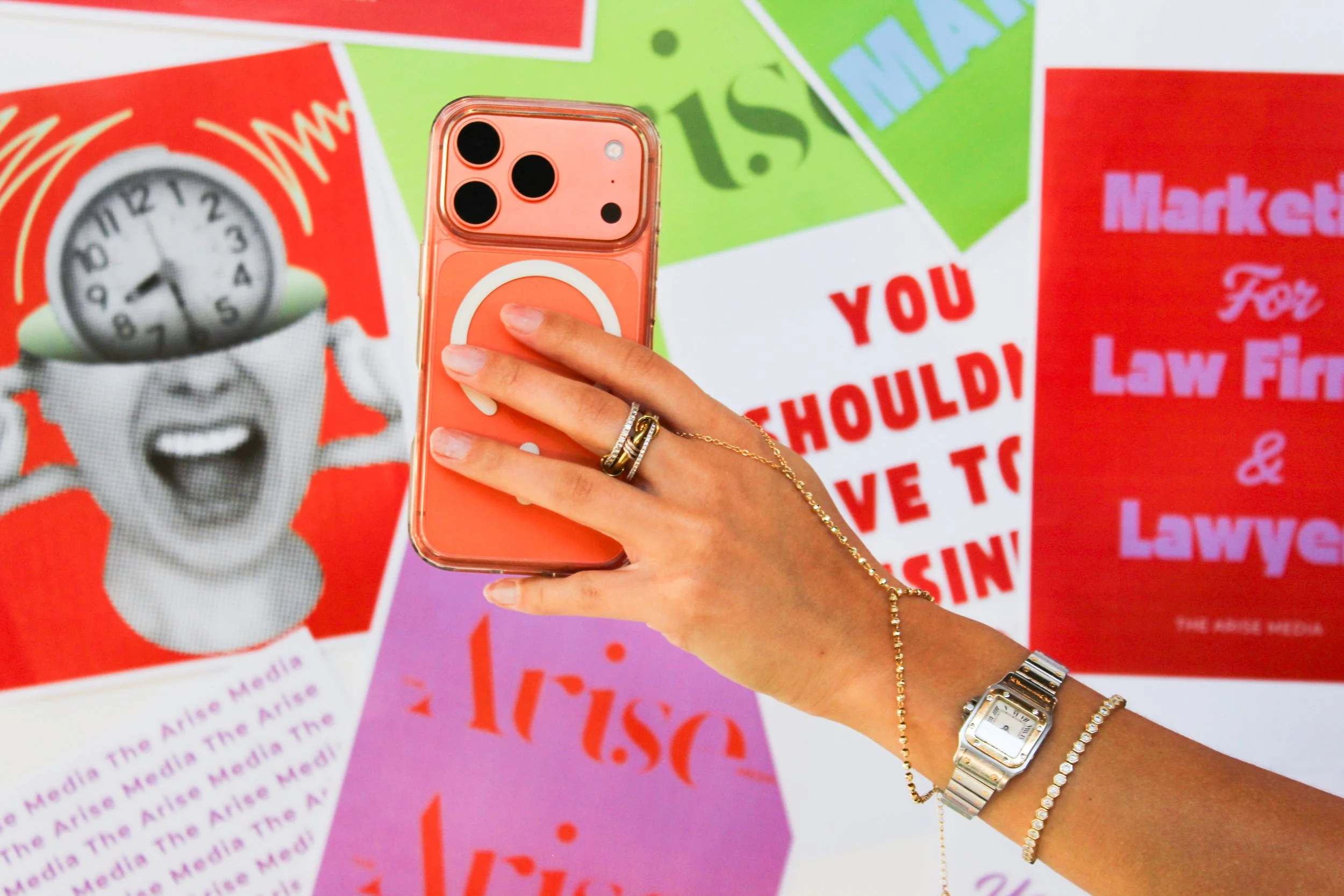 A hand holding a pink cell phone with a pop socket, in front of colorful media protest signs with phrases like "You Should" and "Law".