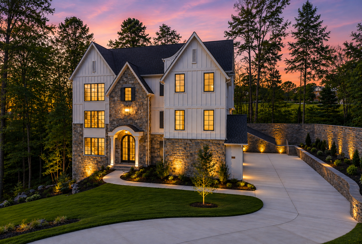 Beautiful modern house with stone and white wooden exterior, illuminated windows, and landscaped front yard with small trees, walking path, and driveway at sunset. Governors Club, Chapel Hill North Carolina