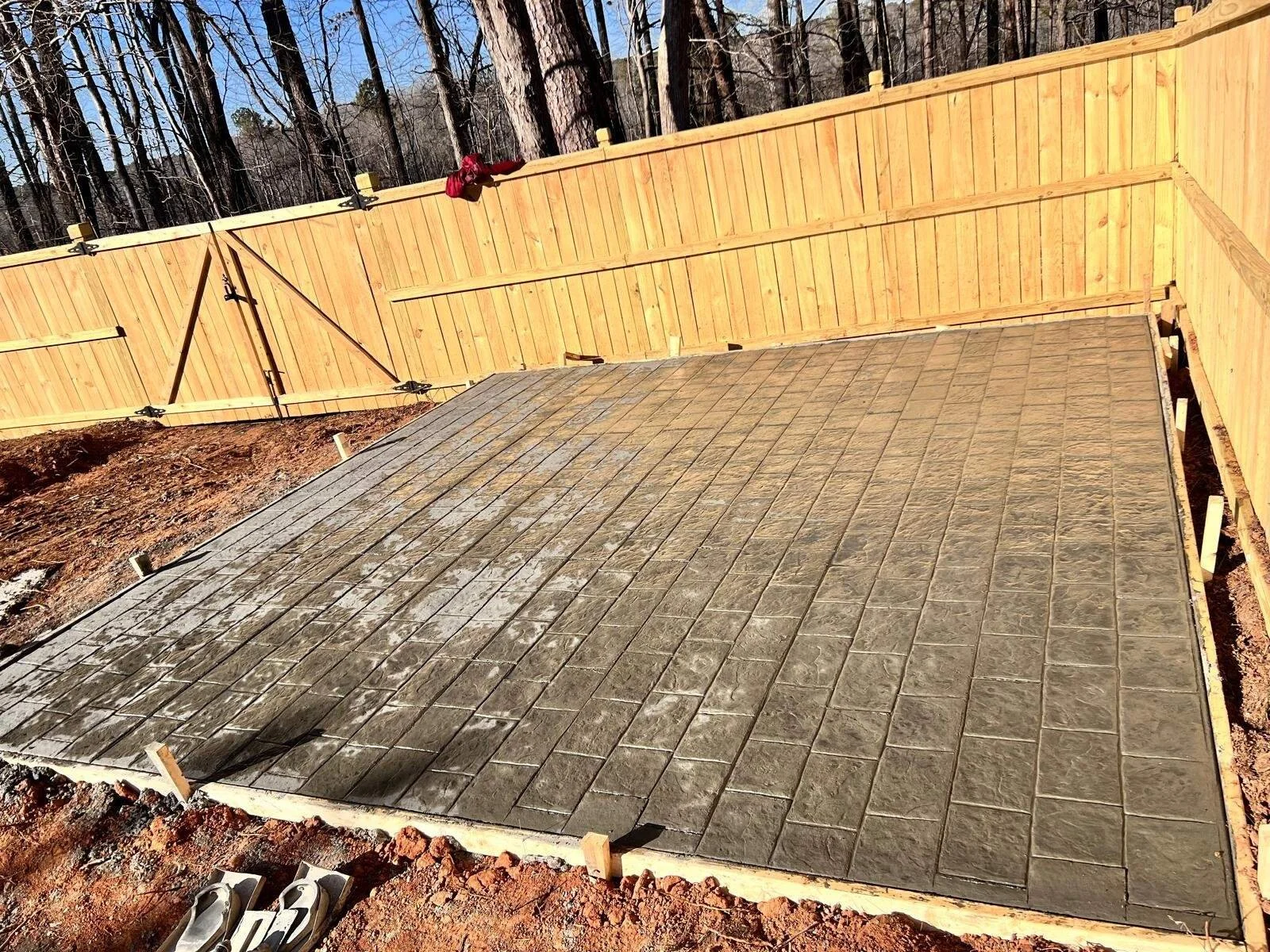 Newly installed stamped concrete patio featuring a rectangular paver pattern, poured next to a wooden privacy fence in a residential backyard in Atlanta.