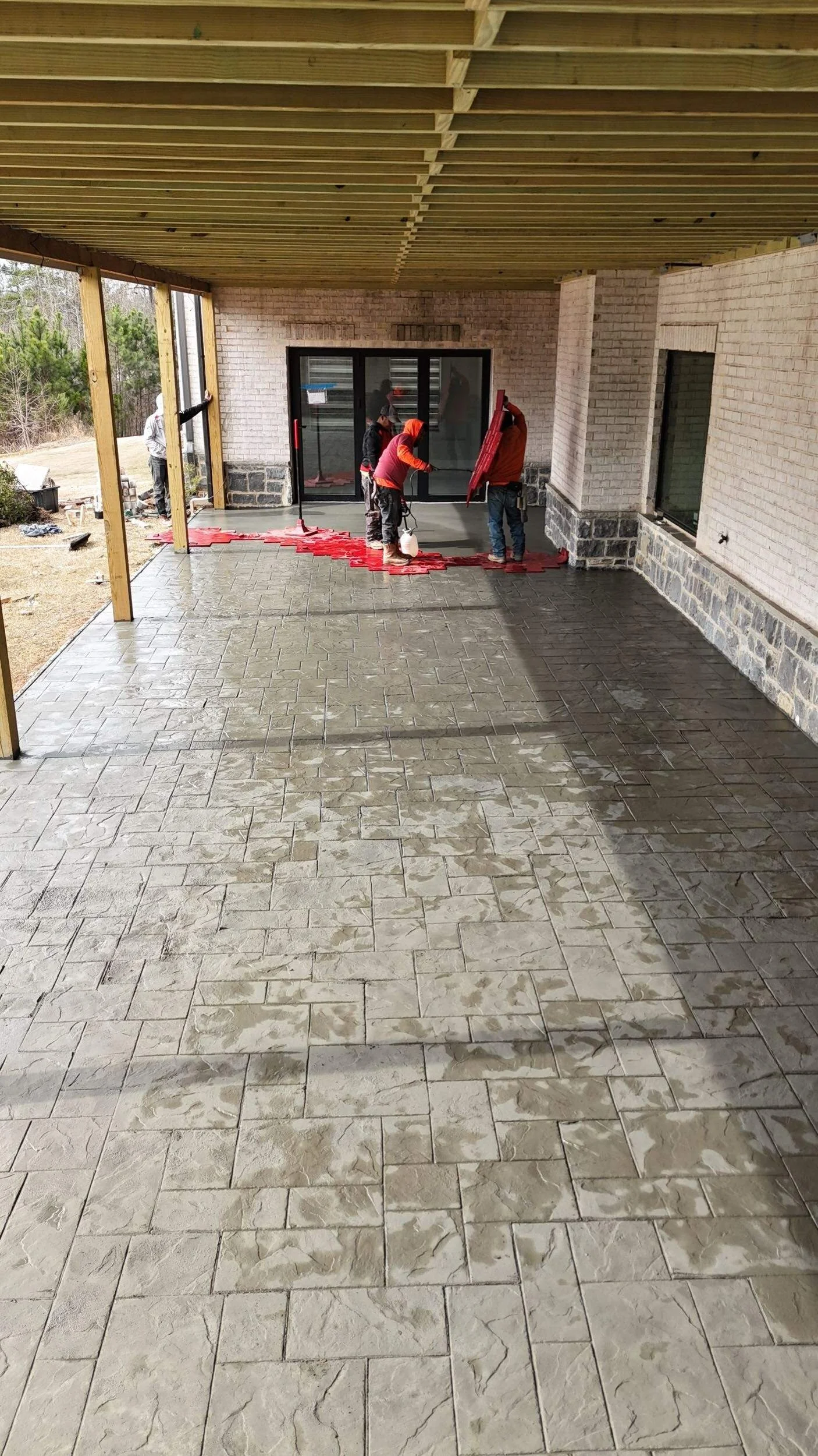 Titan Construction Group crew actively applying large red rubber stamps to a freshly poured concrete patio, creating a custom decorative stone pattern for a residential outdoor living space in Atlanta.
