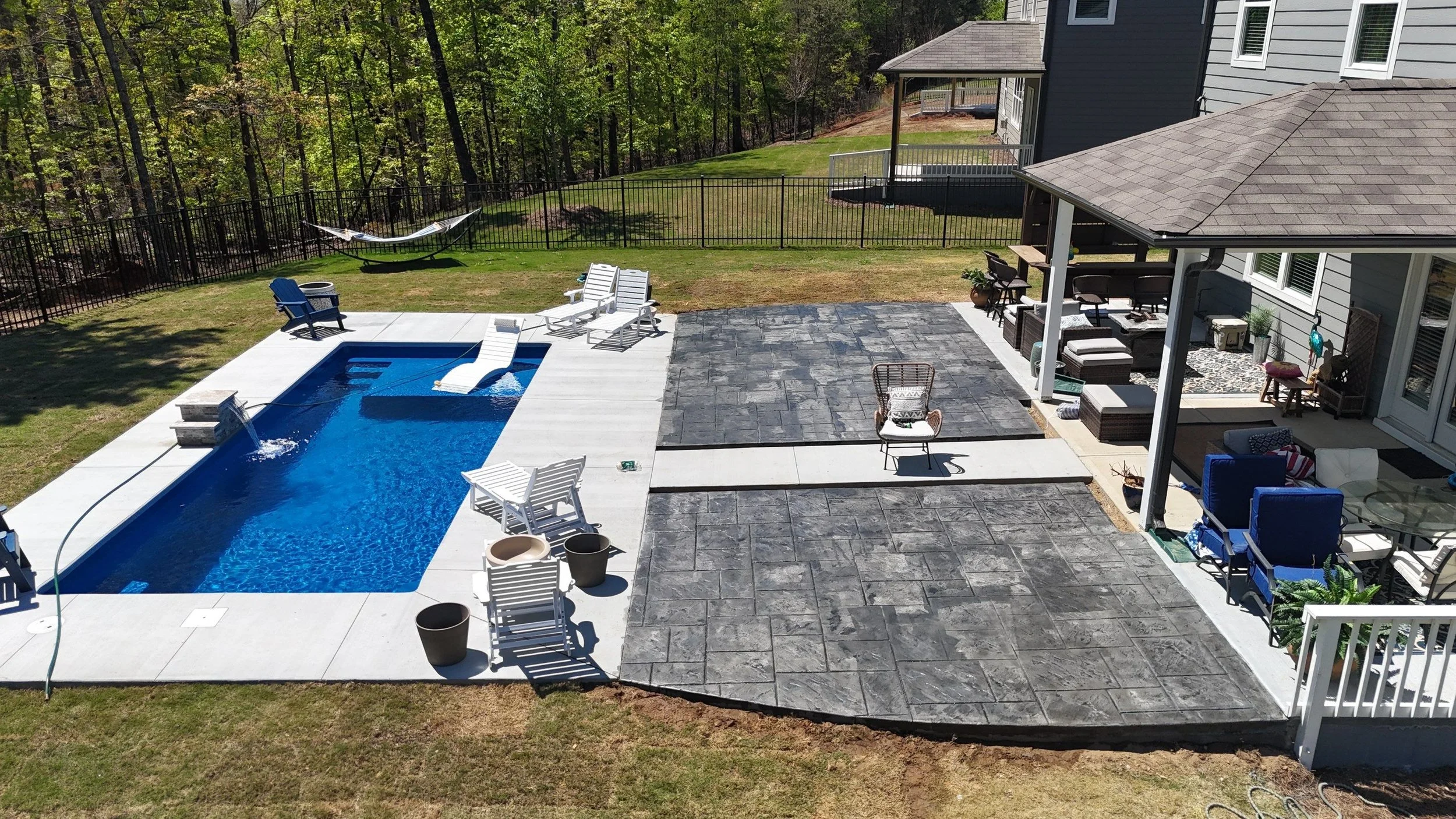 Custom dark grey stamped concrete patio designed to mimic luxury slate stone, poured adjacent to a smooth light concrete pool deck in a residential backyard.
