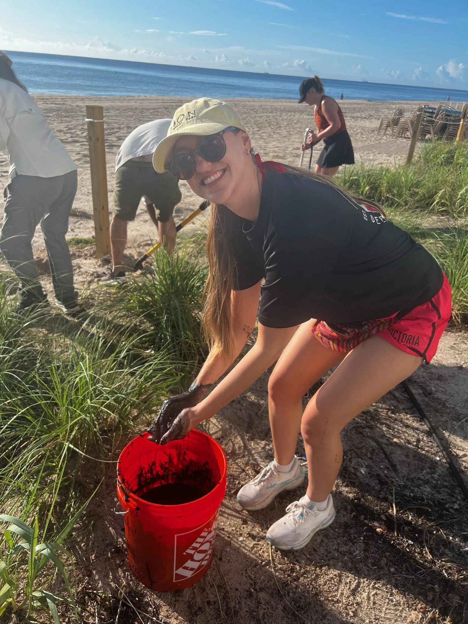 Women bends down next to a bucket of "muck" to be used in dune restoration.