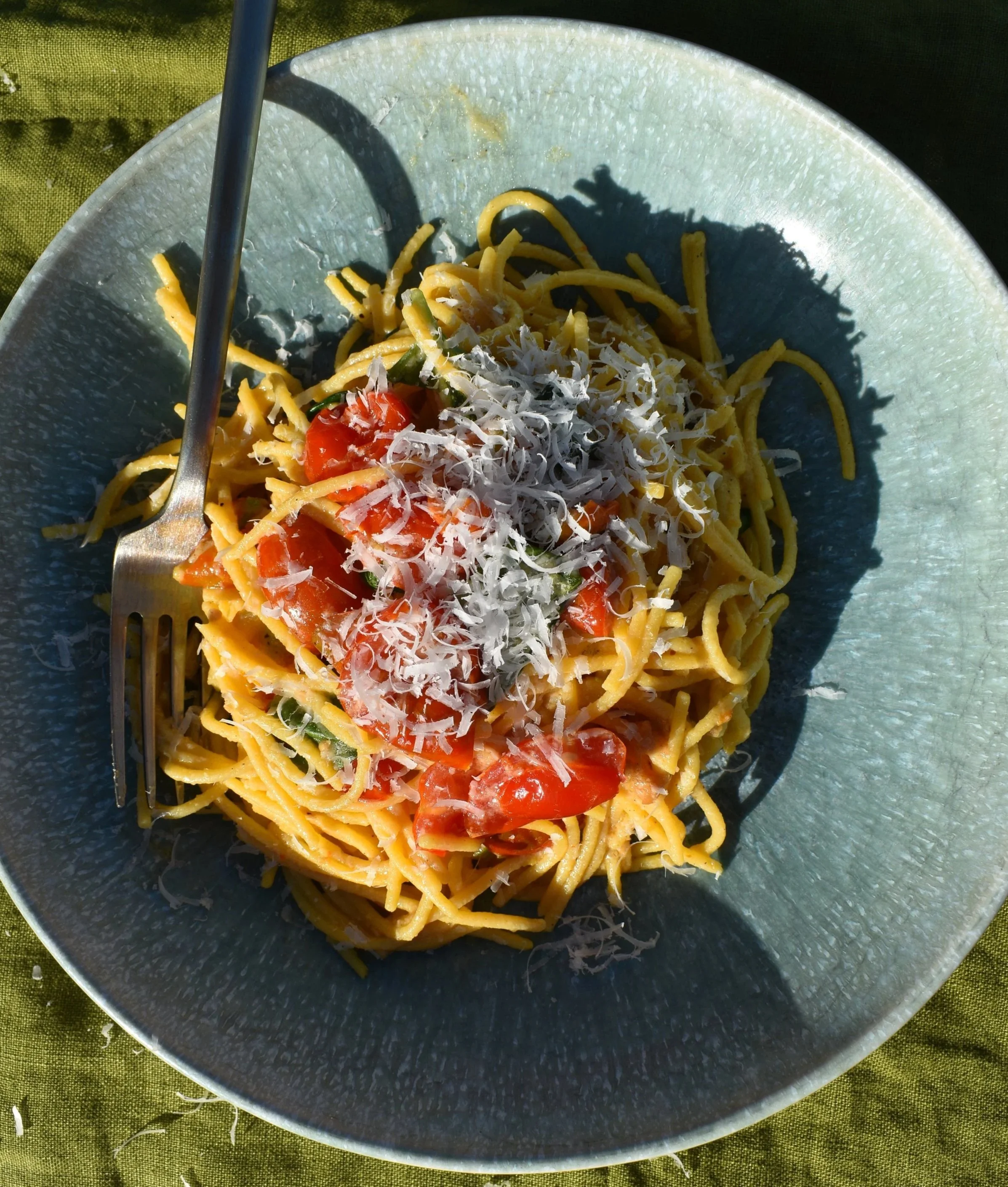 Spaghetti with cherry tomatoes and parmesan cheese in a blue bowl on a green background