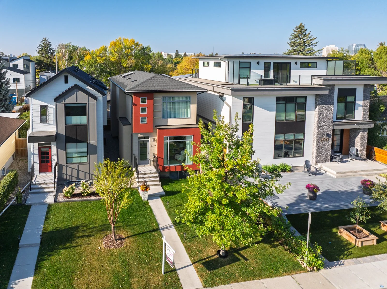 Calgary modern row of houses with landscaped front yards, trees, and outdoor seating areas, under a clear blue sky. One of the property Michele Gole, Exp realty, has sold.