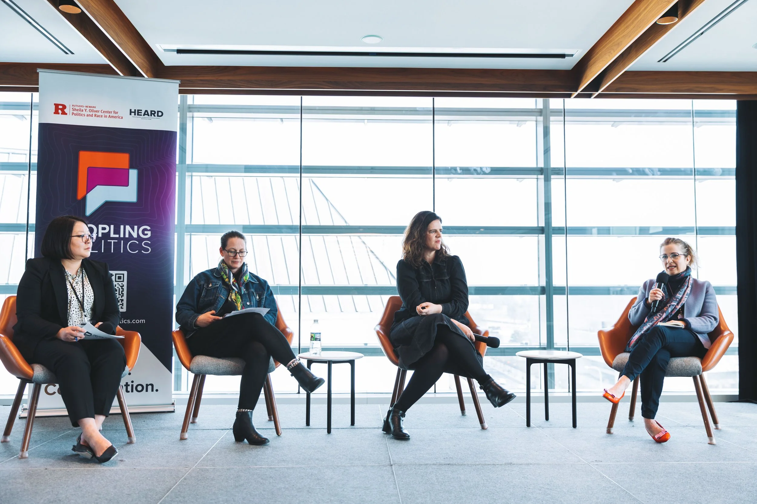Four women seated on stage in conversation, with a vertical banner on the left that reads 'DOPLING POLITICS' and features a speech bubble logo and QR code.