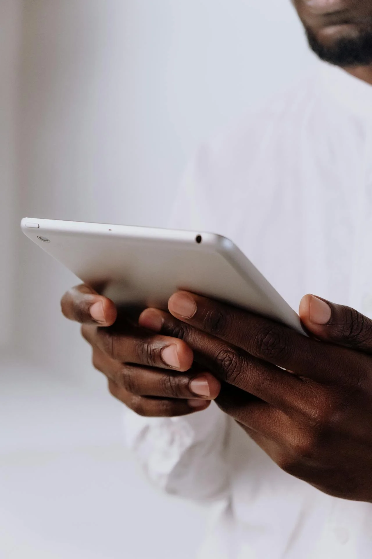 Person holding a white tablet device with a focus on the person's hands and the edge of the tablet.